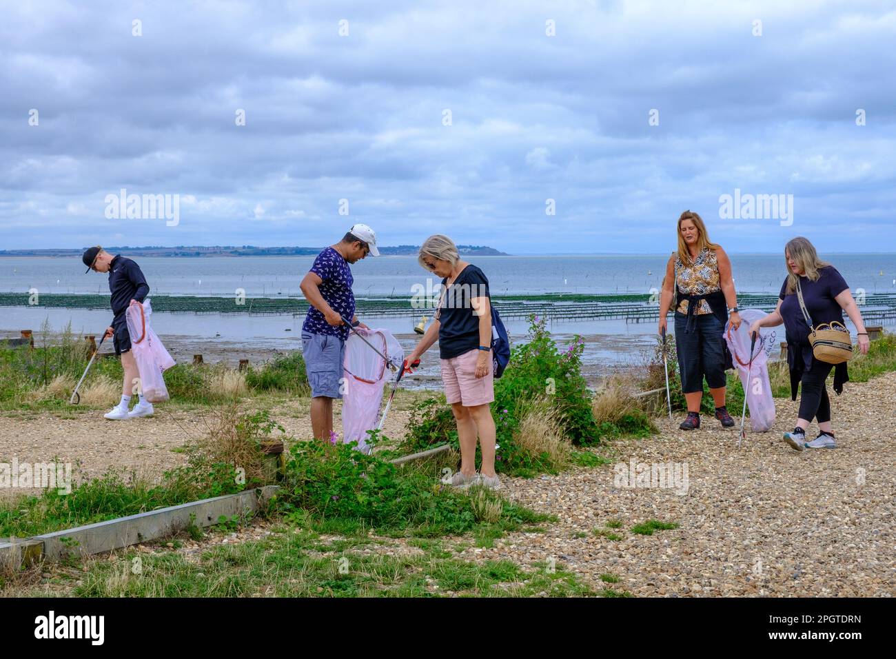 People picking up trash from the beachfront holding trash bags and