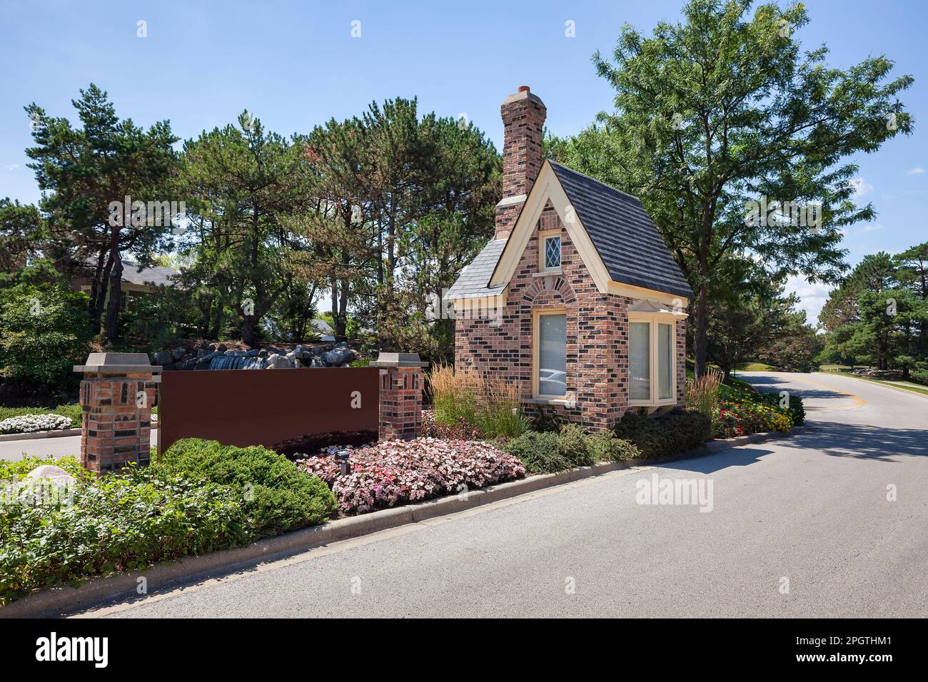 A beautiful landscaped divided entrance with brick pillars, guard house