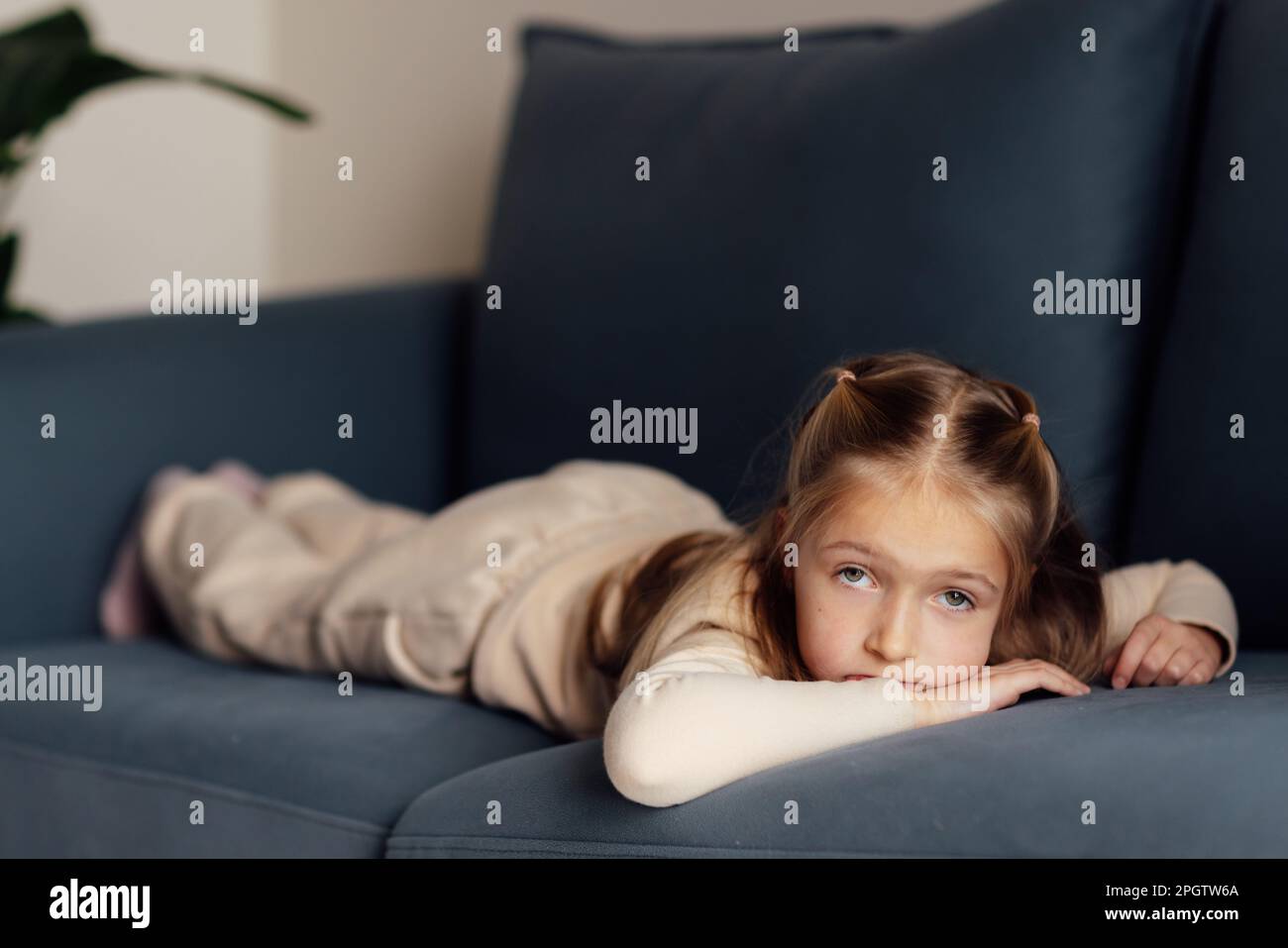 Sad little caucasian girl lying alone on couch in modern apartment and ...