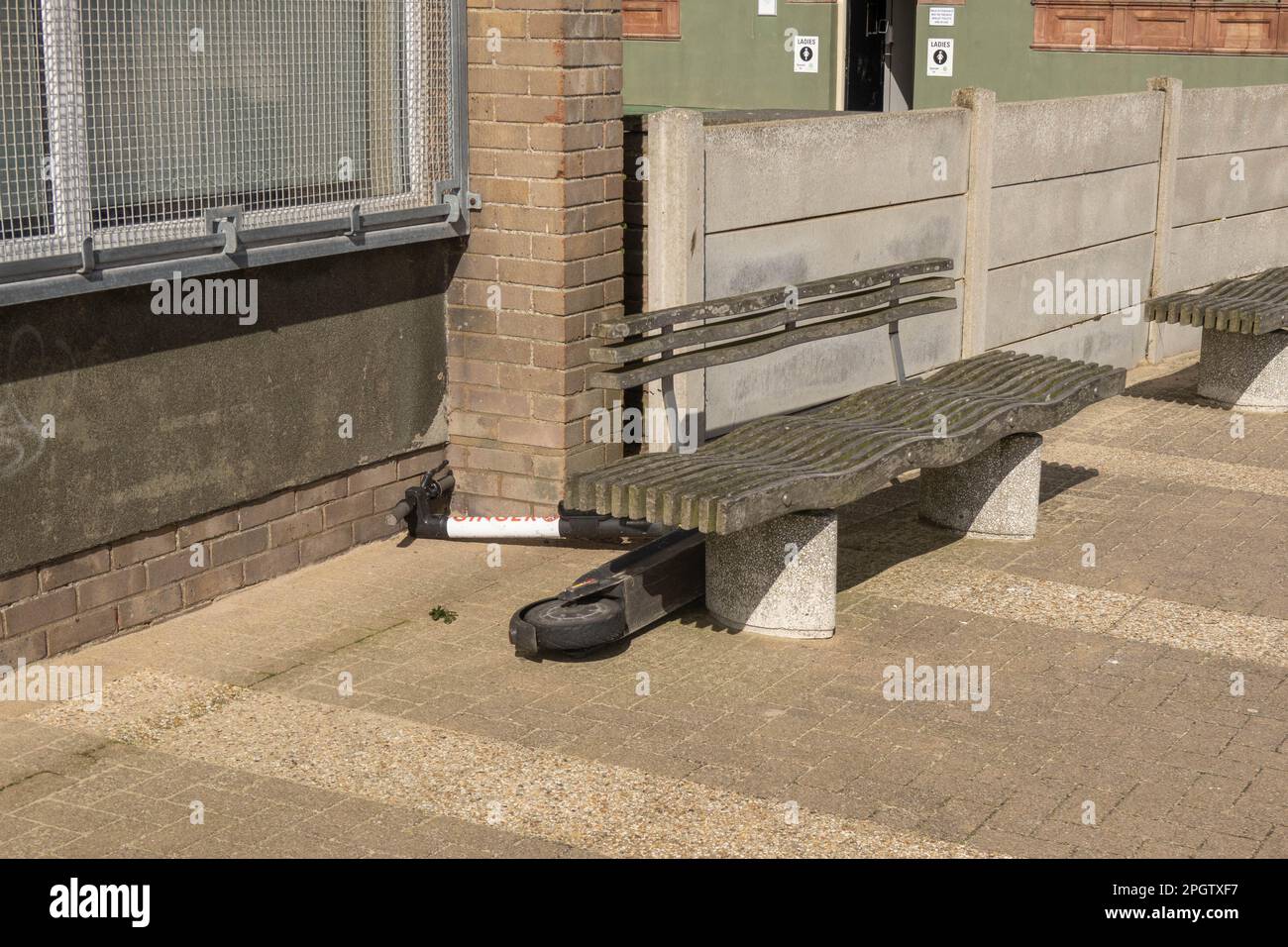 An electric Ginger scooter lying on the promenade behind a bench at