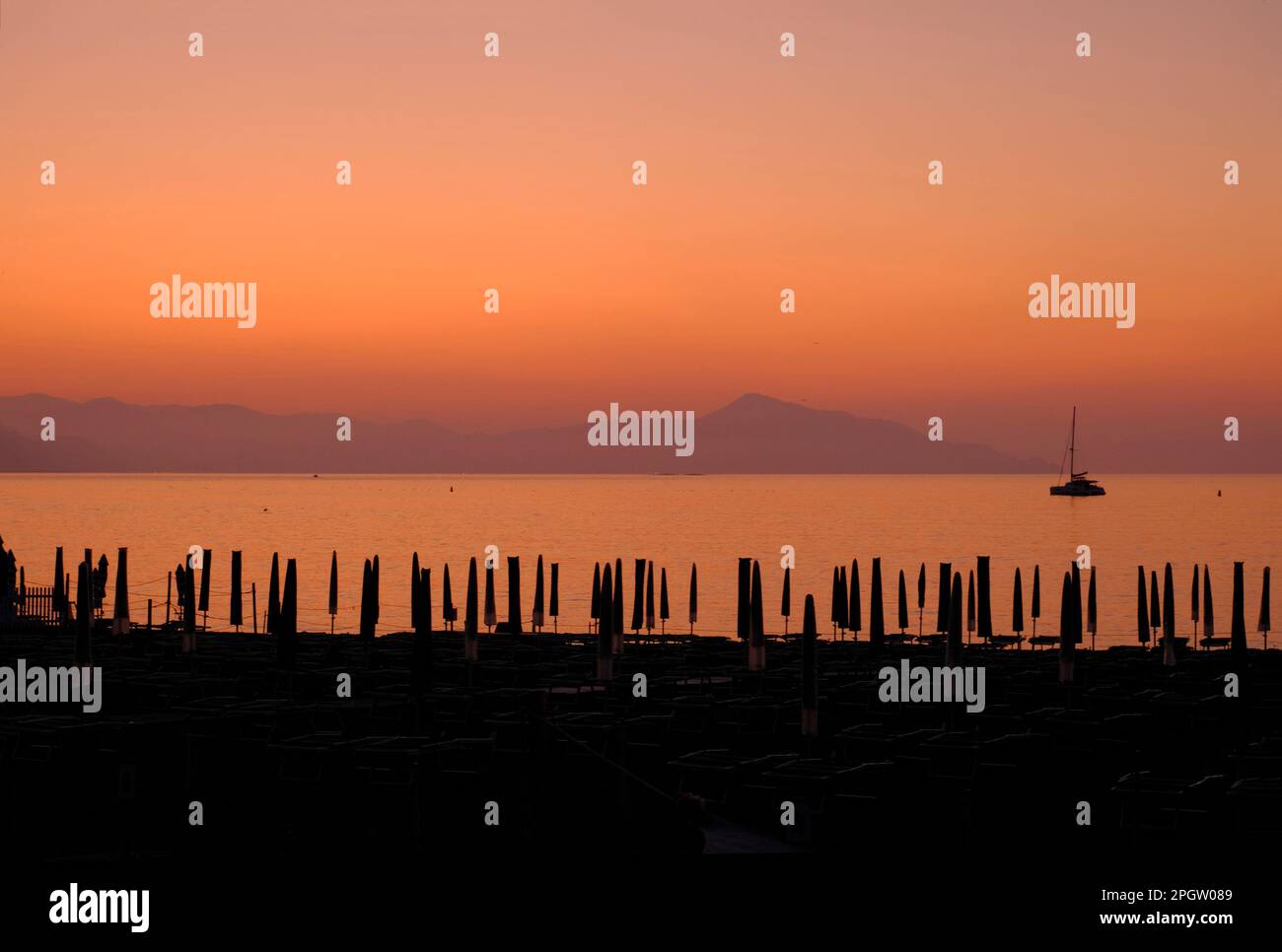 Ship sailing in the sunset sea, across mountains, and sun beds on the beach in Sestri Levante, Liguria, Italy. Summer background Stock Photo