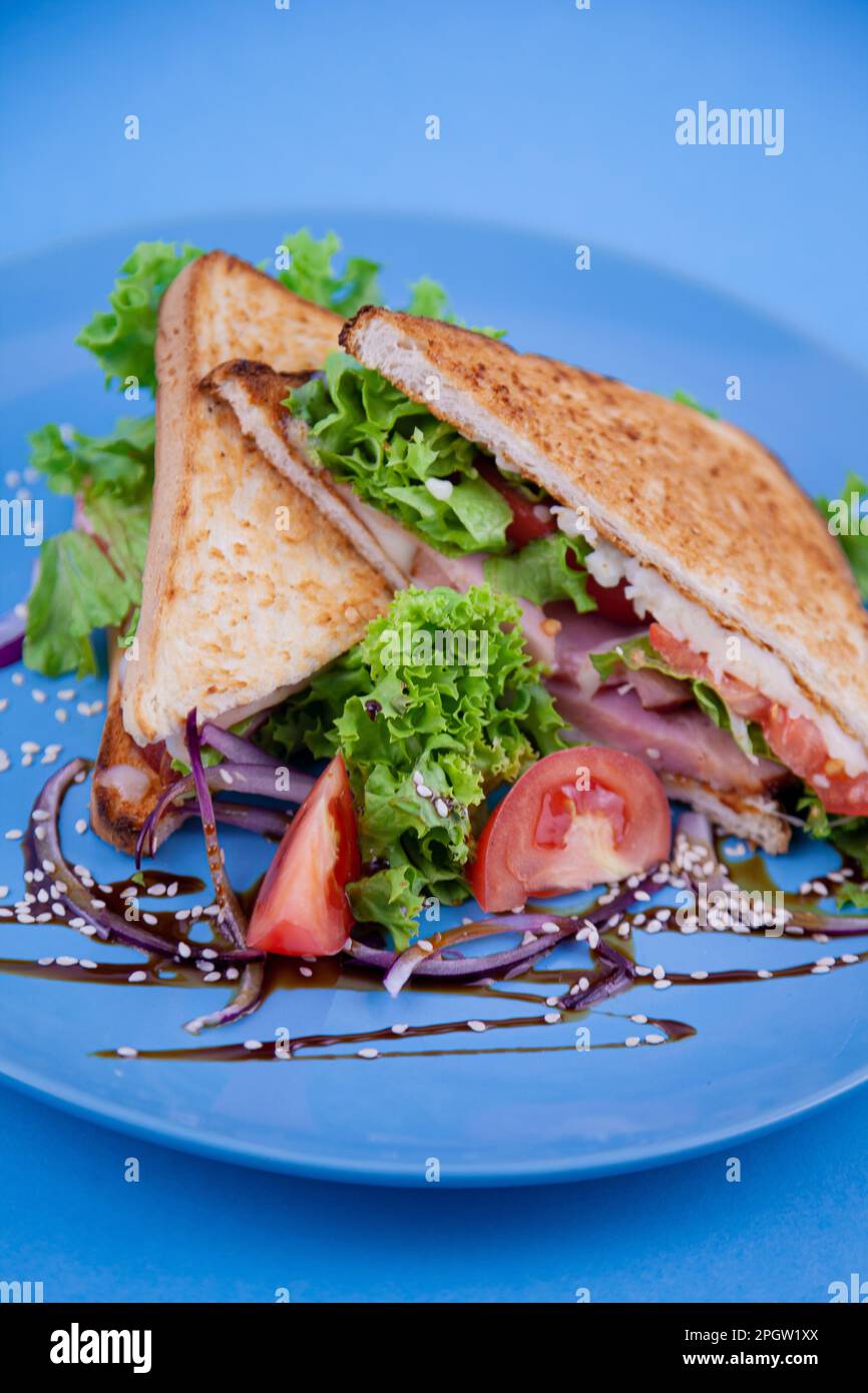 Breakfast sandwich toast with salad. Blue background. Bread, beakon tomatoe on plate top view