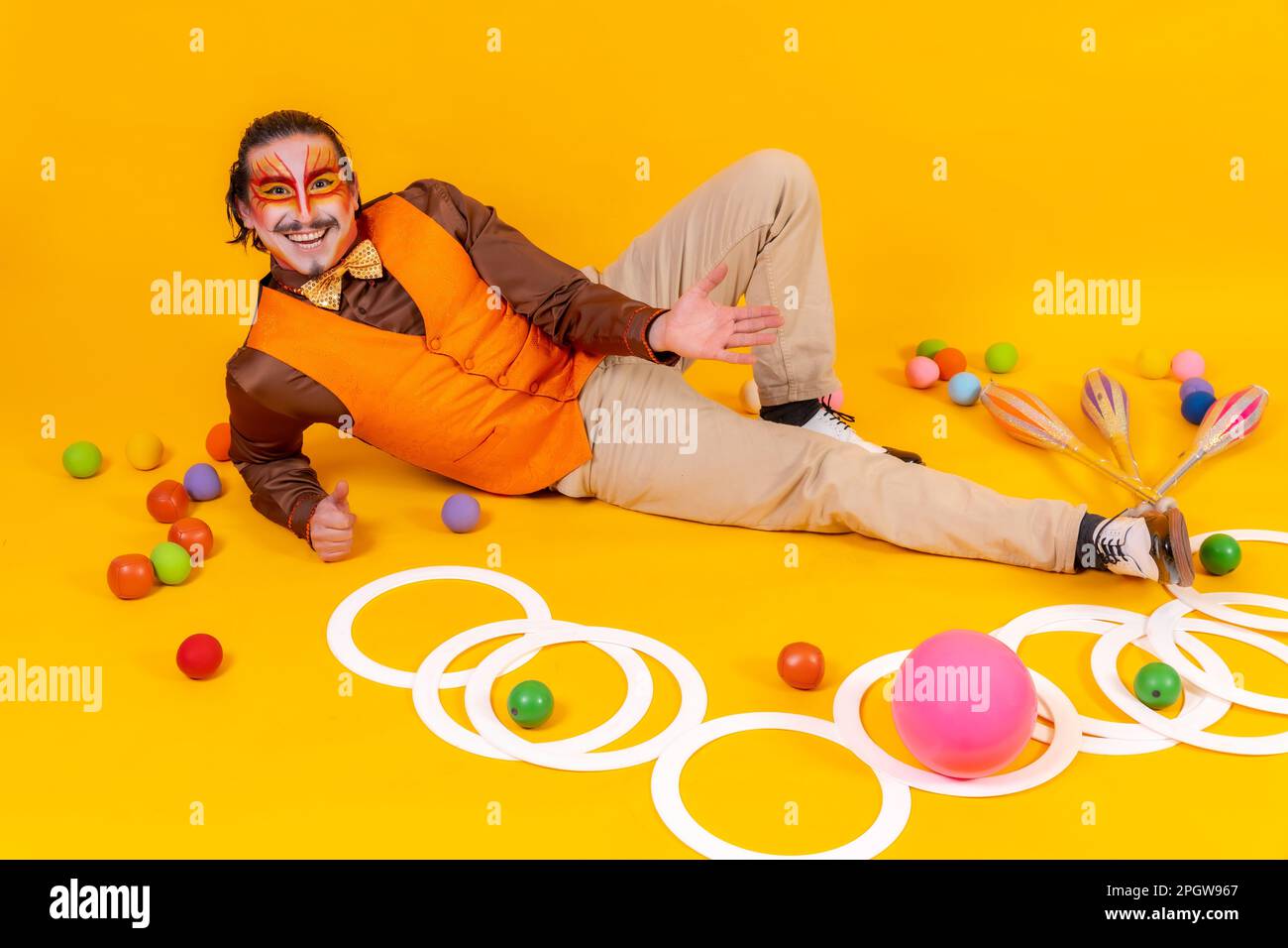 A cheerful circus performer sitting on the ground surrounded by various