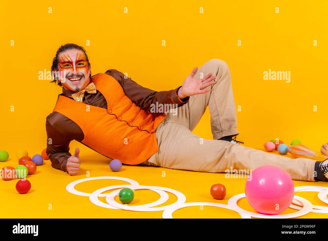A cheerful circus performer sitting on the ground surrounded by various