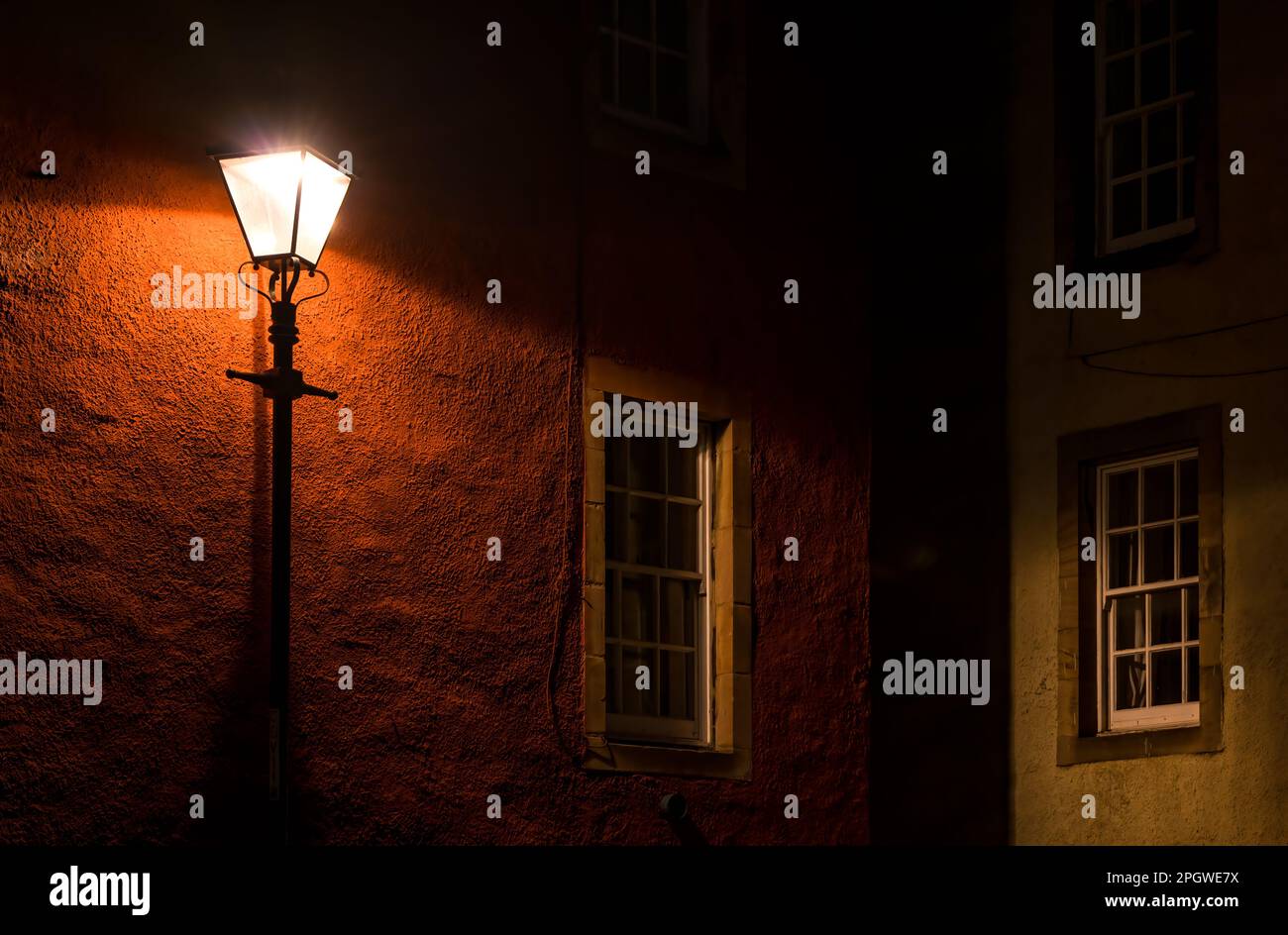 Old fashioned lamp post lit up at night in a dark alley in the Od Town, Edinburgh, Scotland, UK Stock Photo