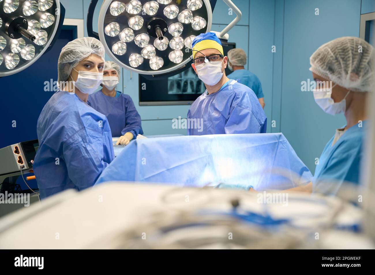 People in surgical gowns and protective masks stand in operating room ...