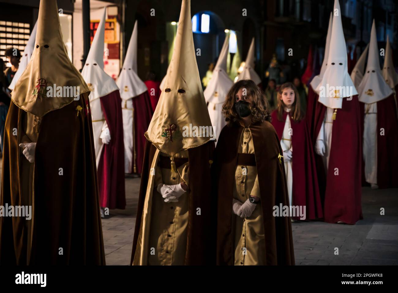 Gandia, Spain -  16 April 2022: Easter procession with hooded people and girls at night at Good Friday Stock Photo