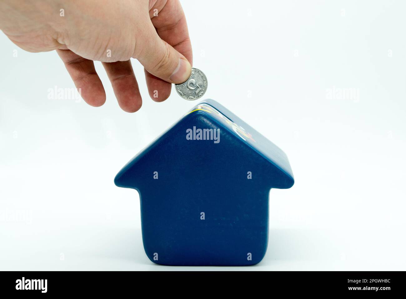 View of a hand throwing a coin into a navy blue piggy bank house on a ...