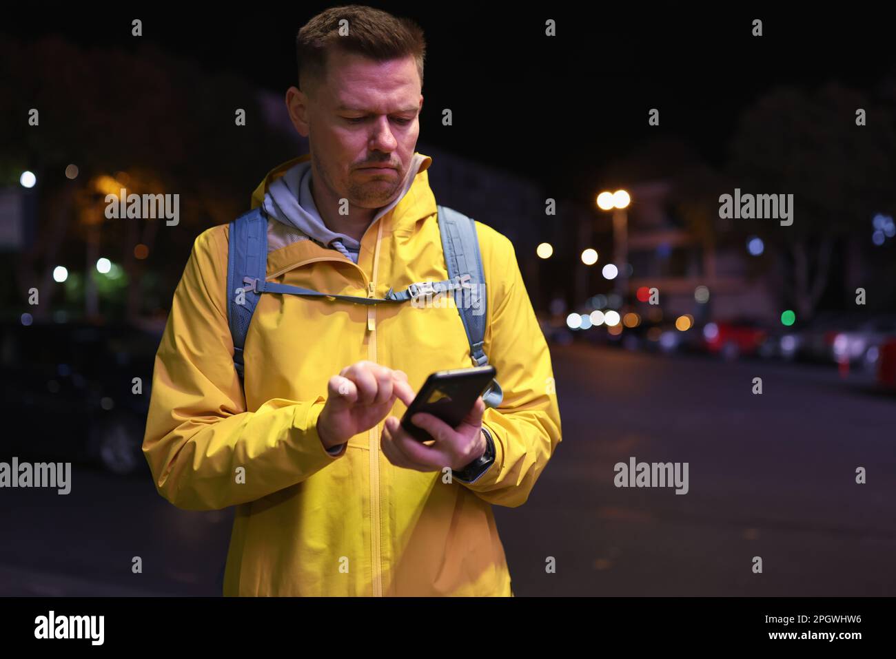 Doubting man in yellow jacket uses phone in night city Stock Photo