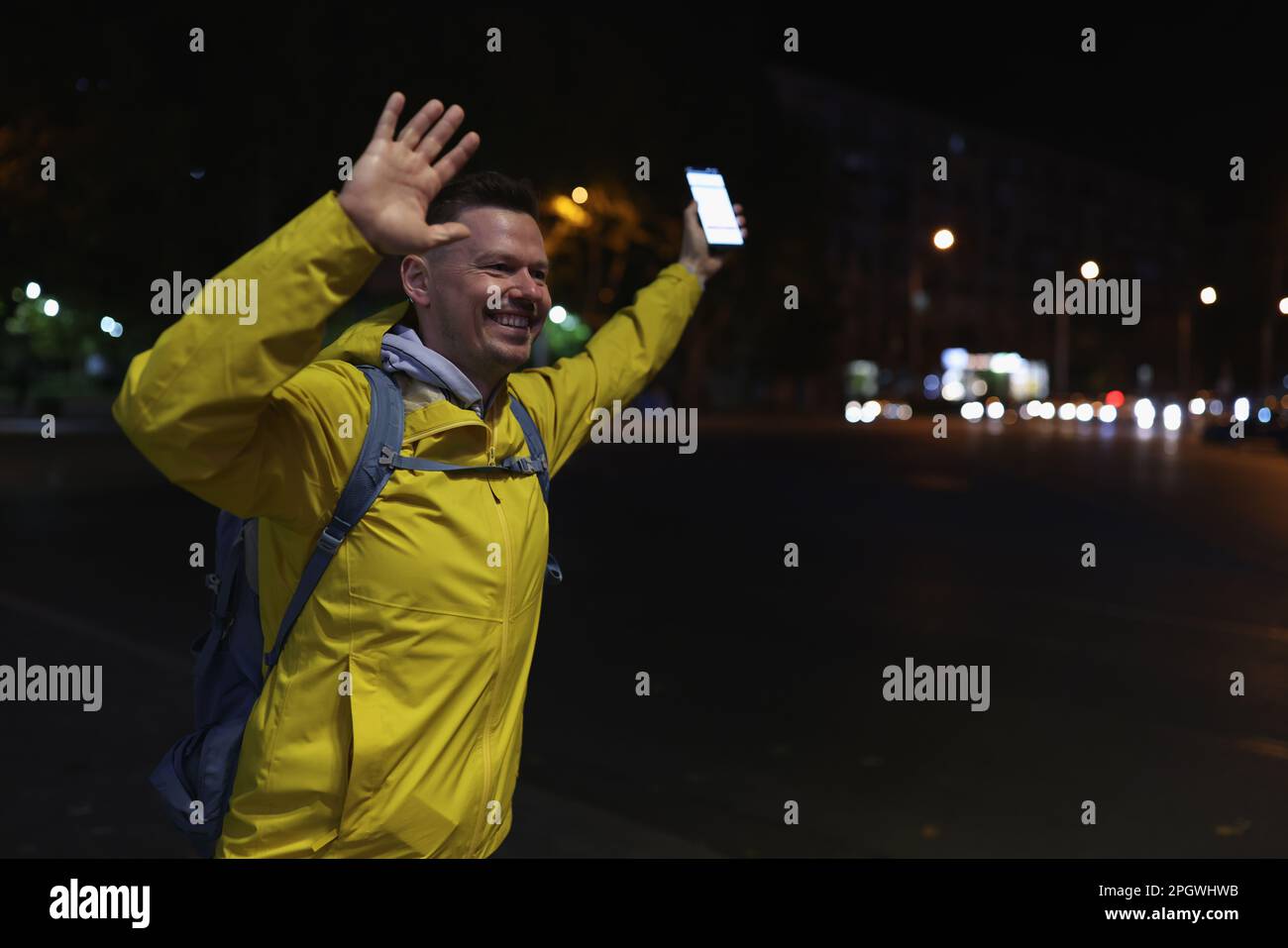 Joyful tourist with cell phone greets friends in night city Stock Photo