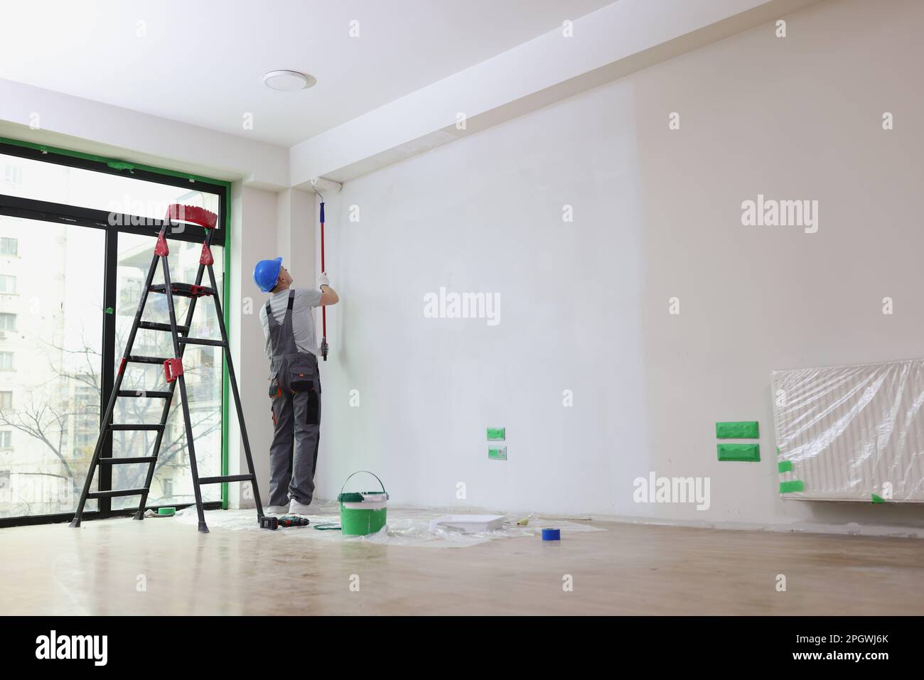 Employee with helmet paints wall with roller in premise Stock Photo