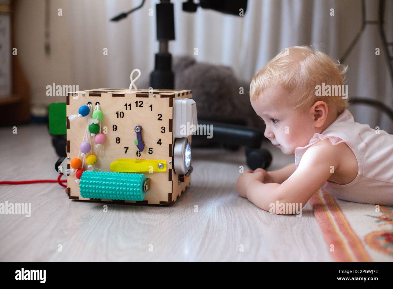 Activity Board. The baby learns the numbers on the clock on the bisiboard. Early development of children with a playful wooden cube toy Montessori. Stock Photo