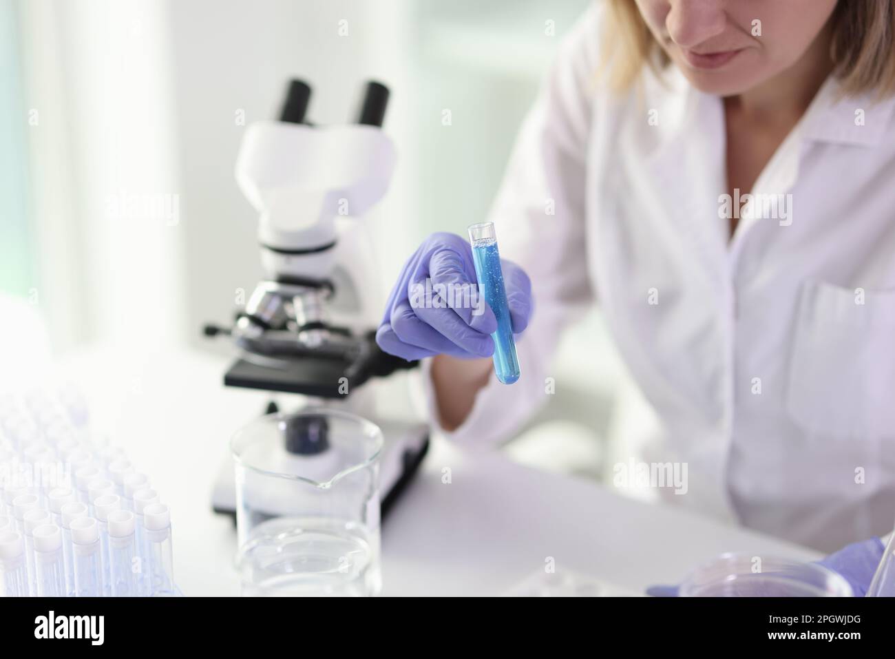 Female worker examines sample in test tube using microscope Stock Photo