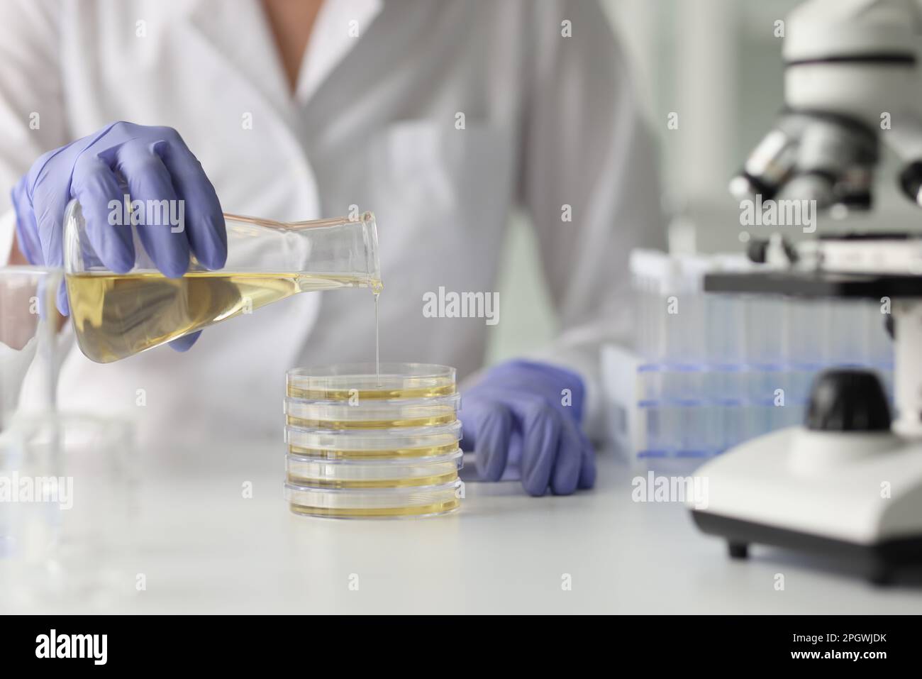 Scientist in gloves pours yellow liquid into glassware Stock Photo