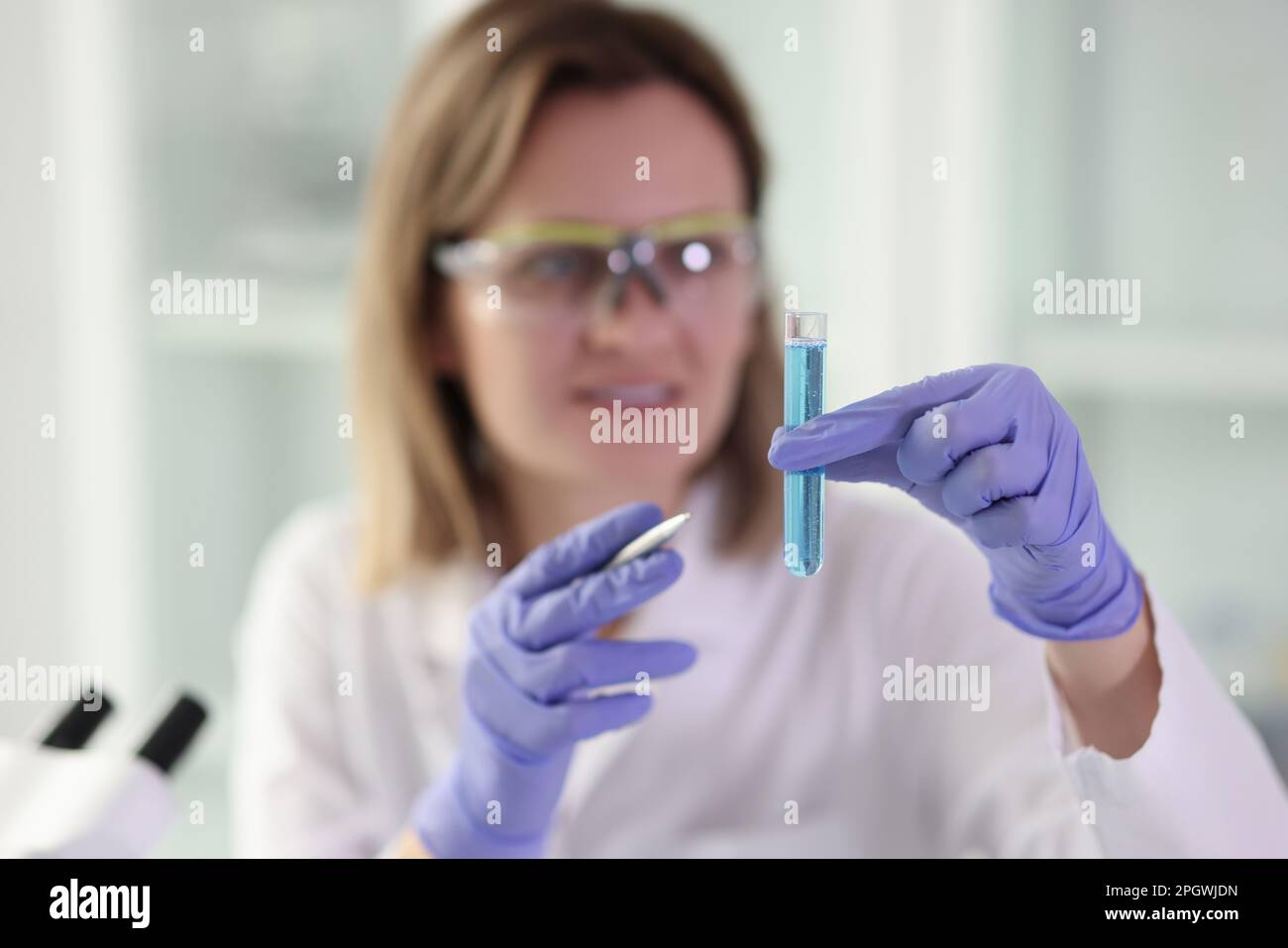 Woman holds glassware with blue chemical liquid for research Stock Photo