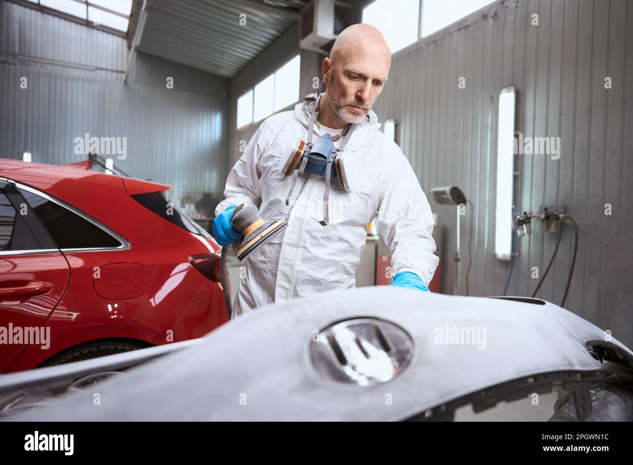 Auto repair shop employee grinds with unpainted car bumper Stock Photo