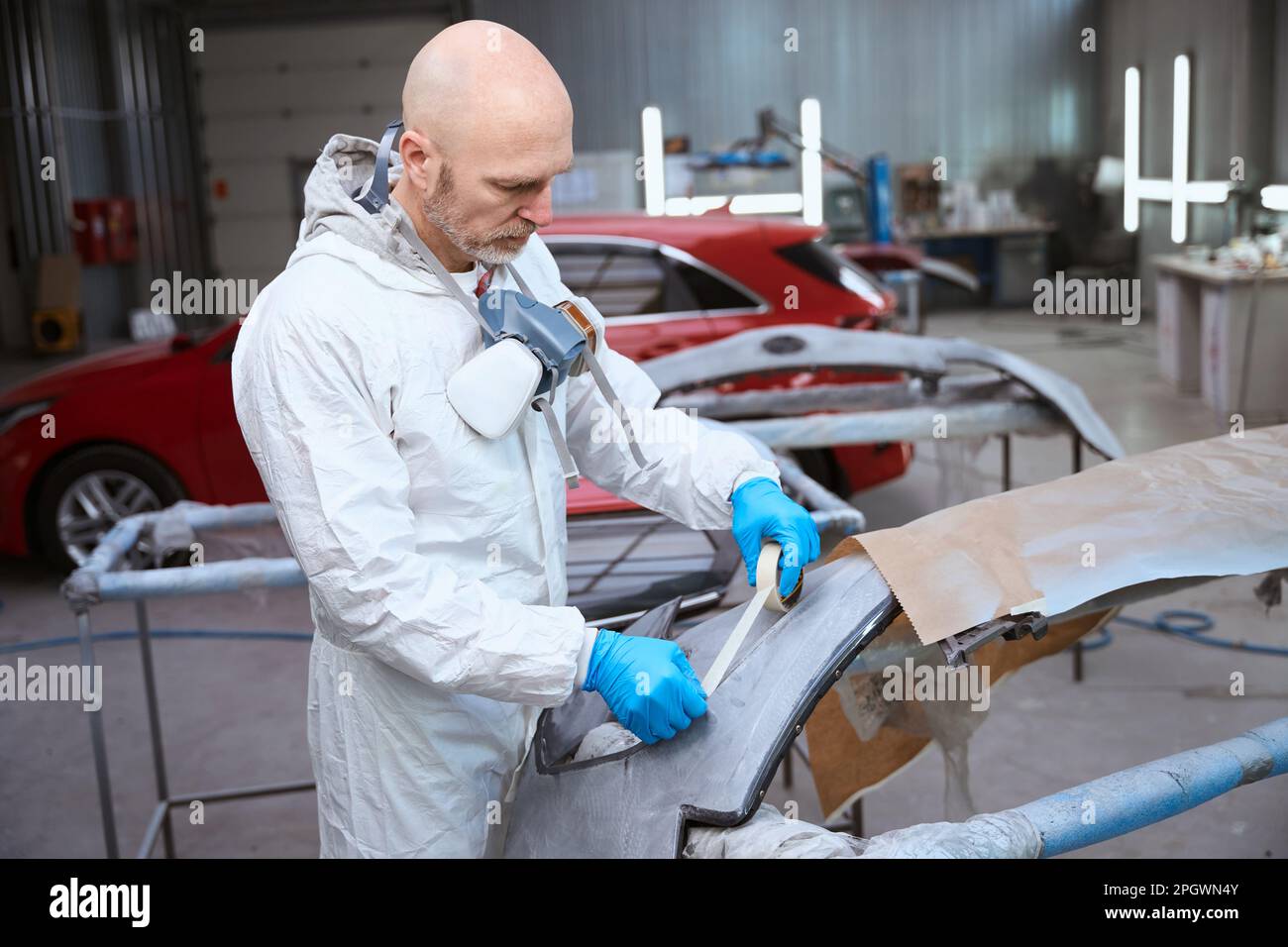 Auto repair shop worker prepares car bumper for painting Stock Photo