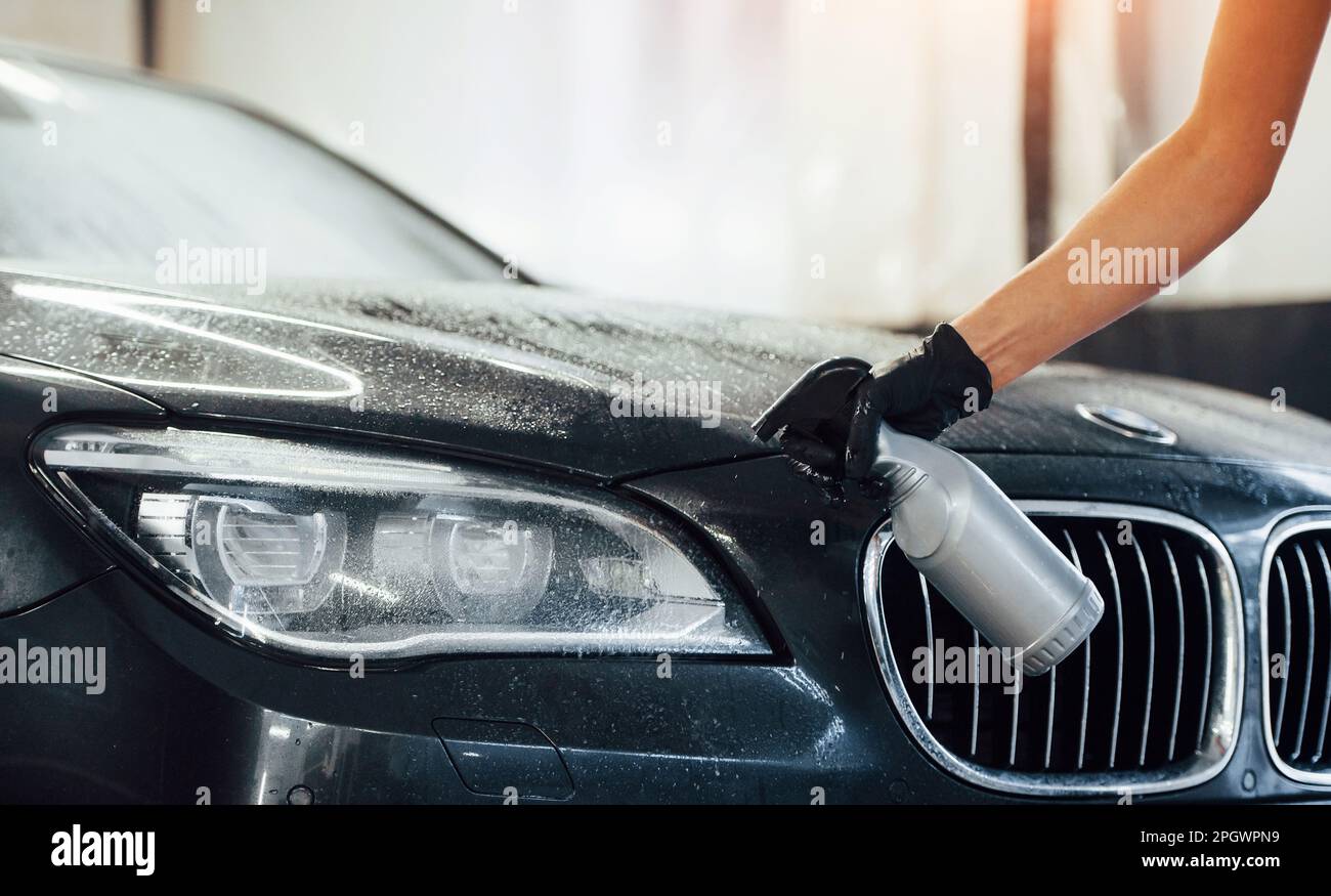 Spraying the vehicle. Modern black automobile get cleaned by woman
