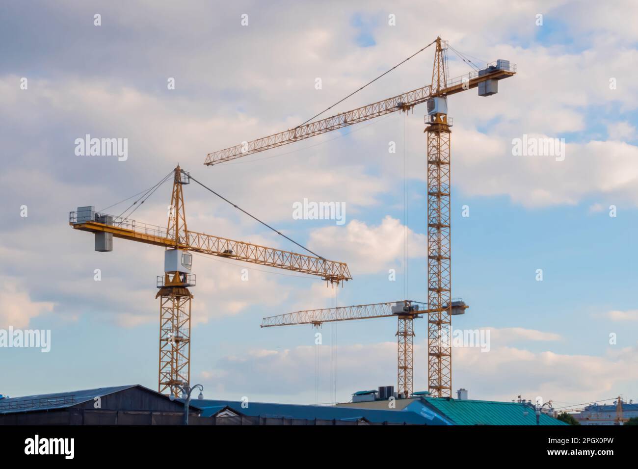 Three yellow tower construction cranes against cloudy sky Stock Photo