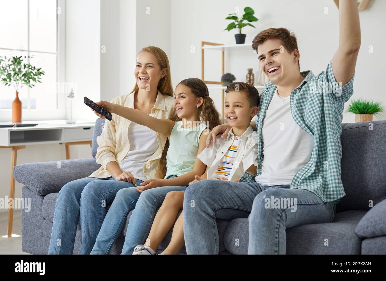 Happy family are sitiing on couch smiling and watching TV together at home in weekend. Stock Photo
