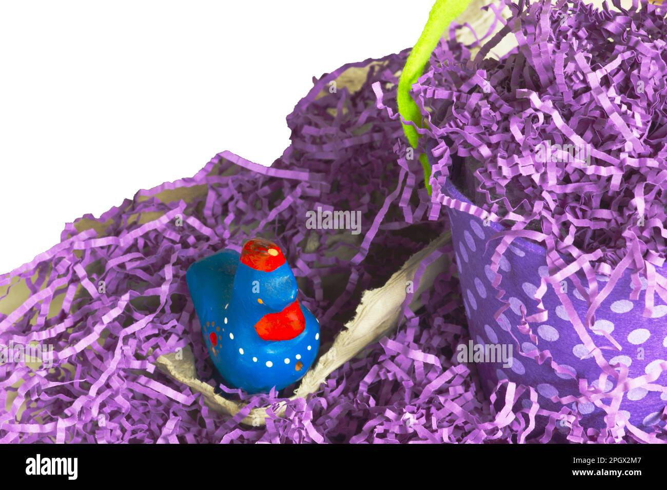 Easter grass with purple polkadot basket or pail placed by a chicken figure. Text space comes with image. Chicken is kitten on an egg carton. Stock Photo