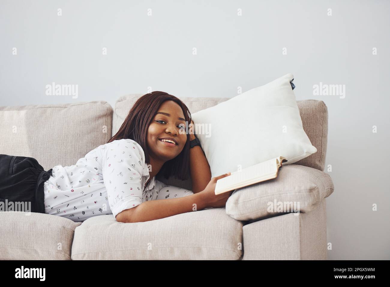 Positive african american woman in white shirt lying down on sofa with ...