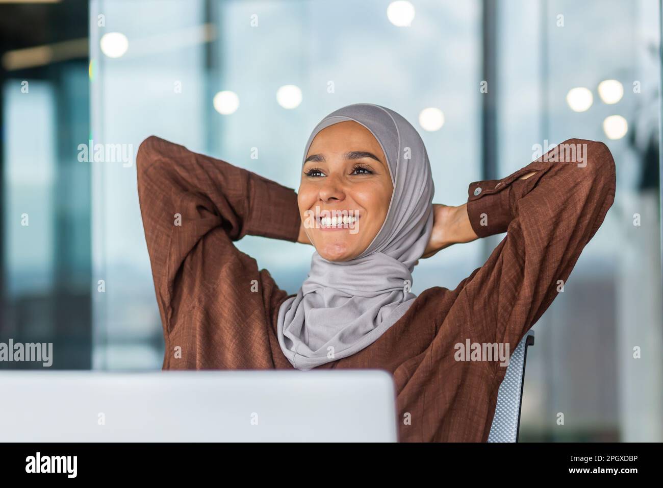 A dreamy and smiling young Arab woman in a hijab is sitting in the ...