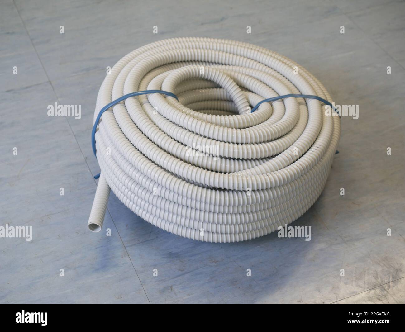 Roll of Gray PVC Corrugated Flexible  Wire Loom Conduit on light blue floor Stock Photo