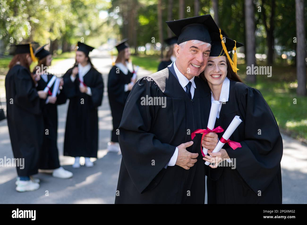A group of graduates in robes outdoors. An elderly man and a young