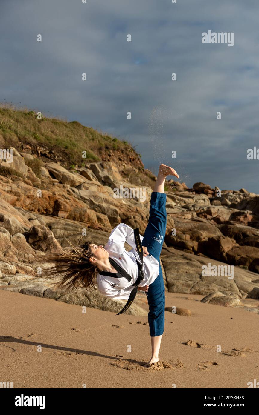 woman doing taekwondo on the beach giving a kick Stock Photo
