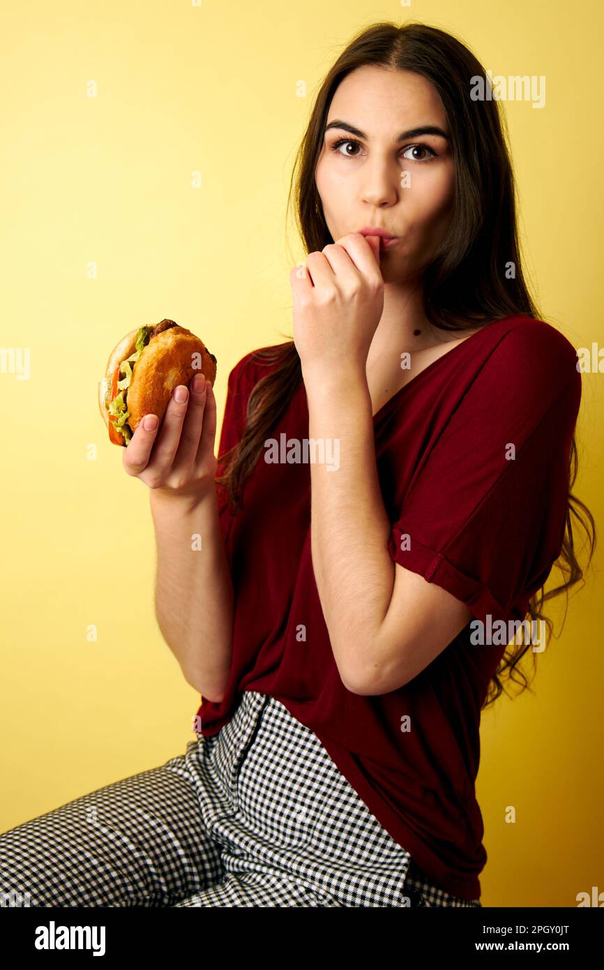 Woman licking her fingers after taking a bite of a hamburger in her hand Stock Photo