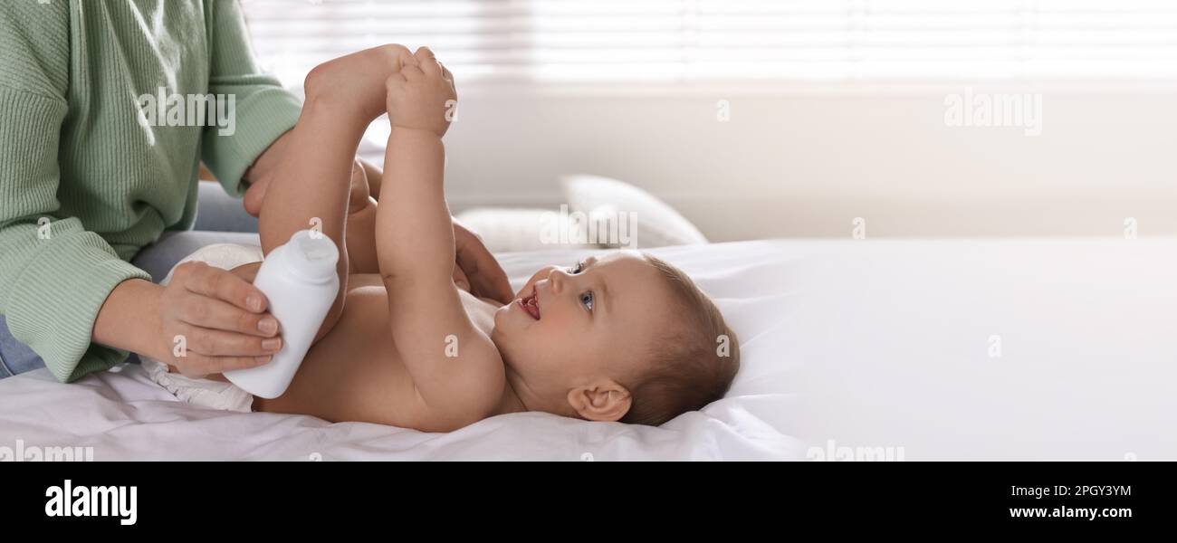 Mother with bottle of dusting powder near her cute baby at home. Banner ...