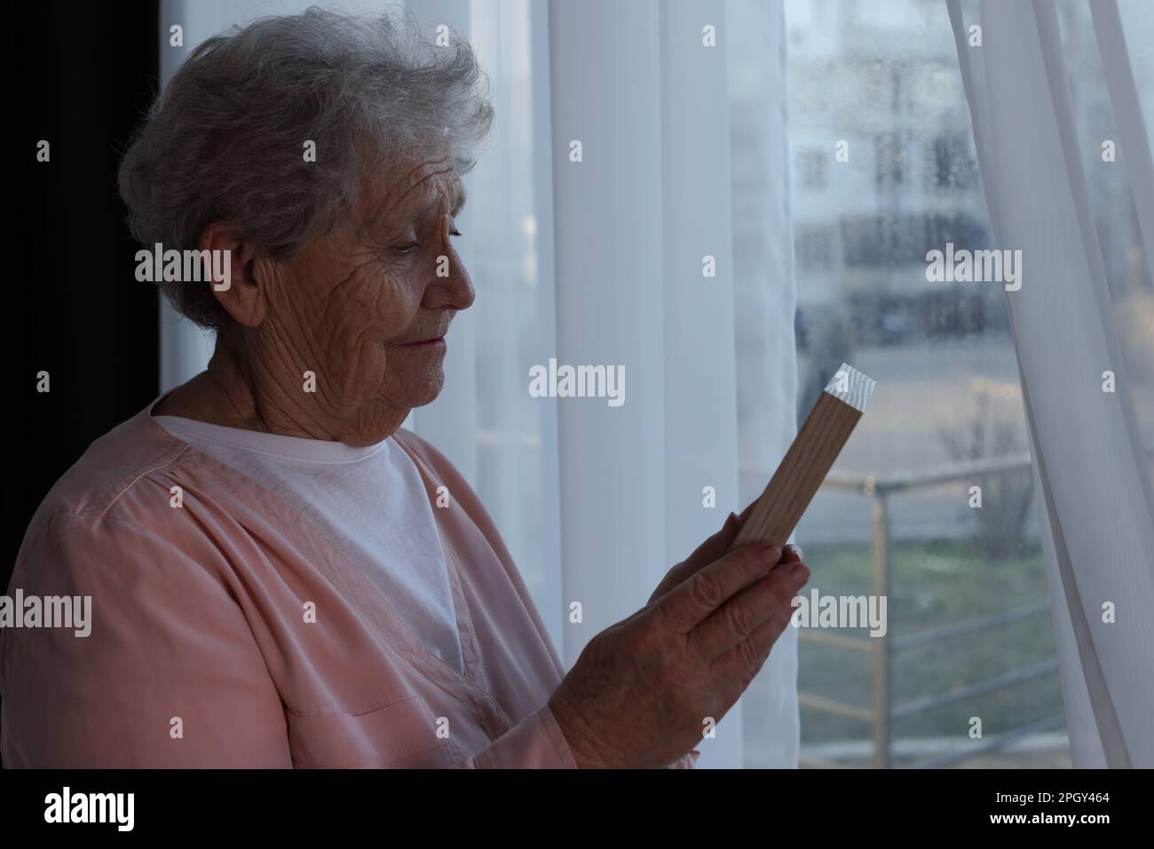 Elderly woman with photo frame near window indoors. Loneliness concept Stock Photo