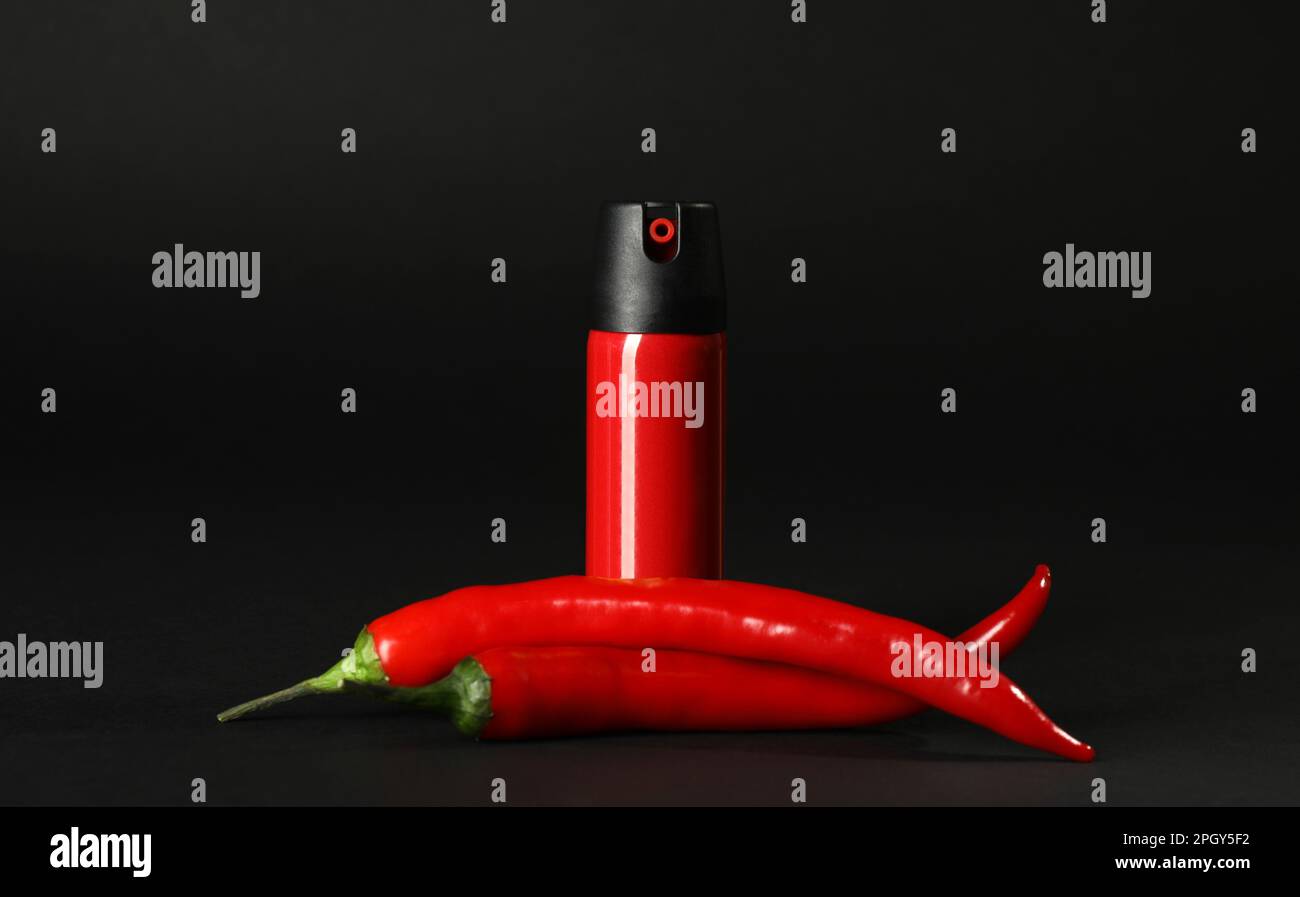 Bottle of gas pepper spray and fresh chili peppers on black background