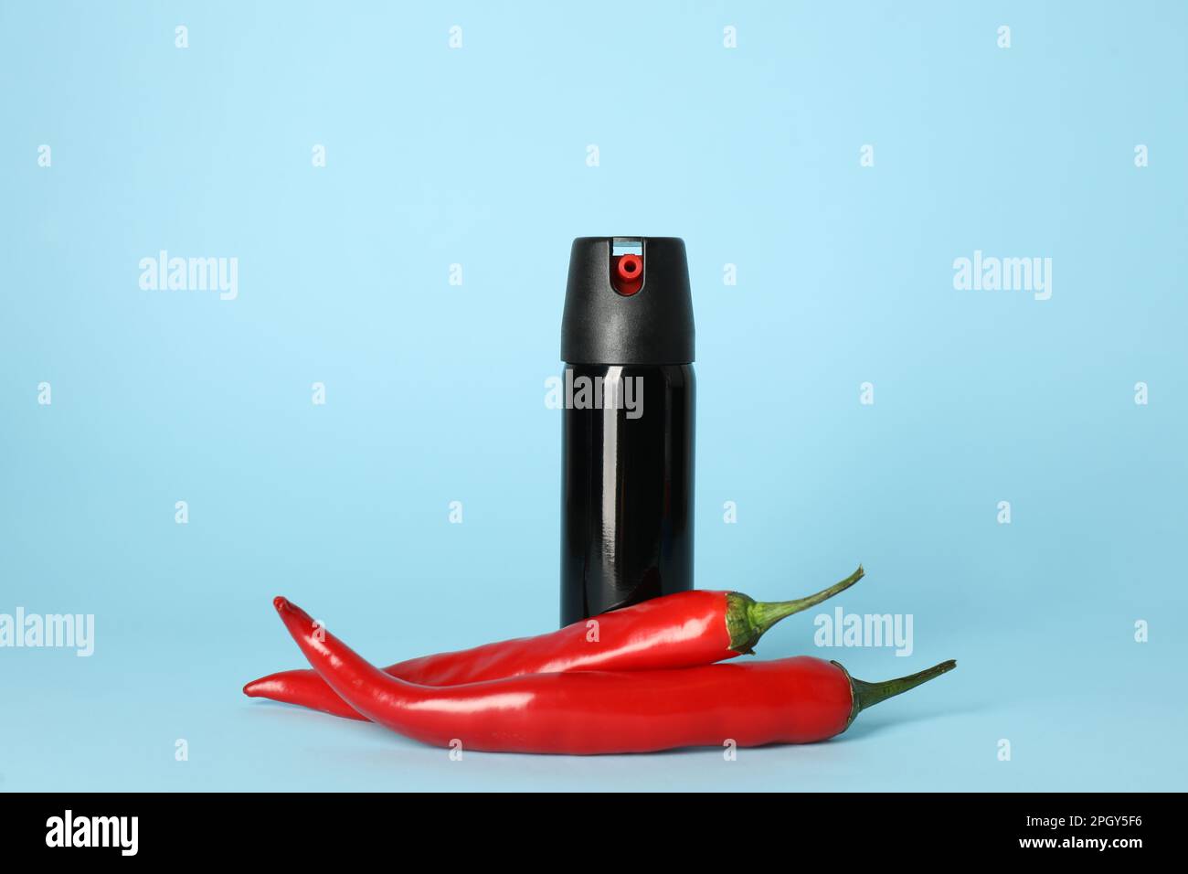 Bottle of gas pepper spray and fresh chili peppers on light blue