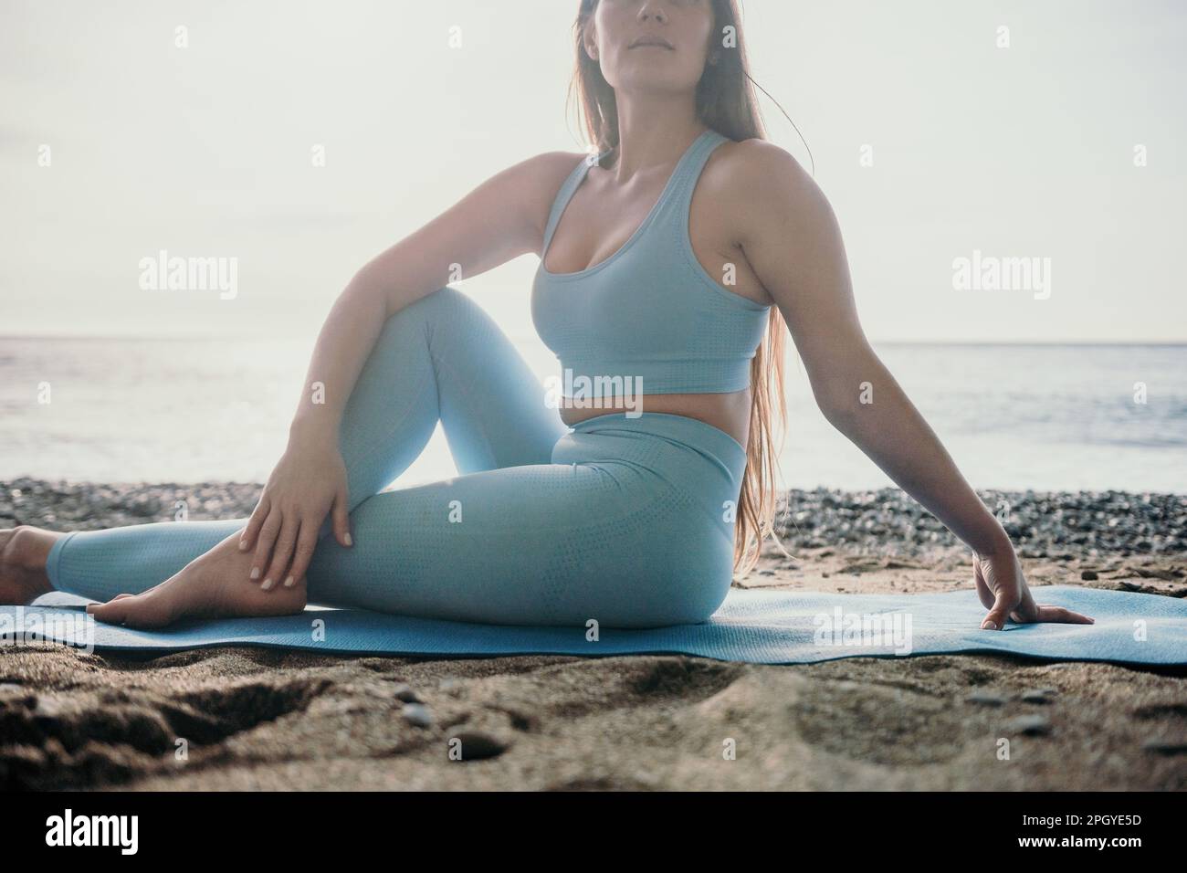 Woman sea pilates. Sporty happy middle aged woman practicing fitness on beach near sea, smiling active female training on yoga mat outside, enjoying Stock Photo