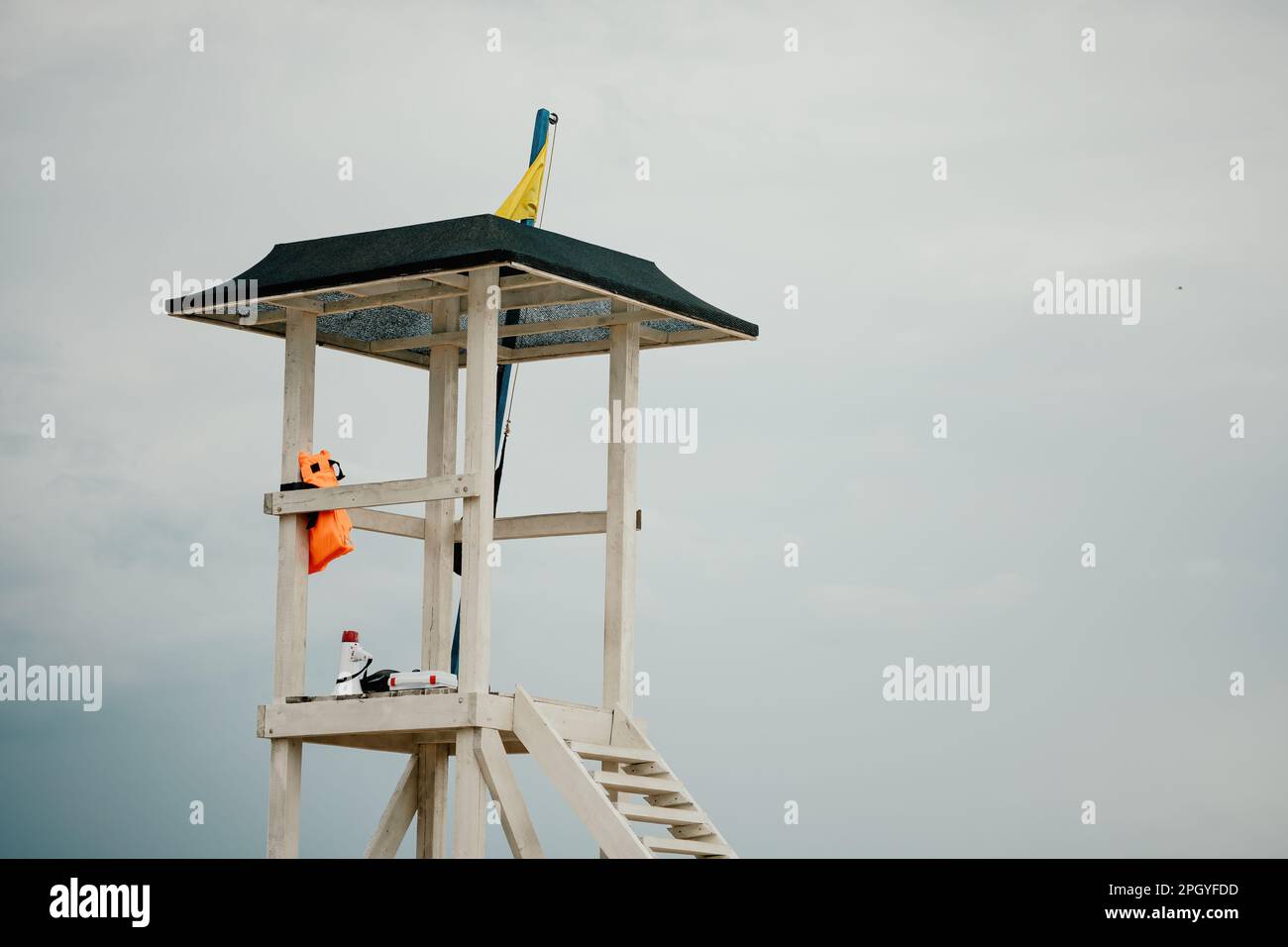 Empty white lifeguard tower with a yellow flag on the beach in windy weather. Beach lifeguard tower with yellow flag indicator. Nobody. Holiday Stock Photo