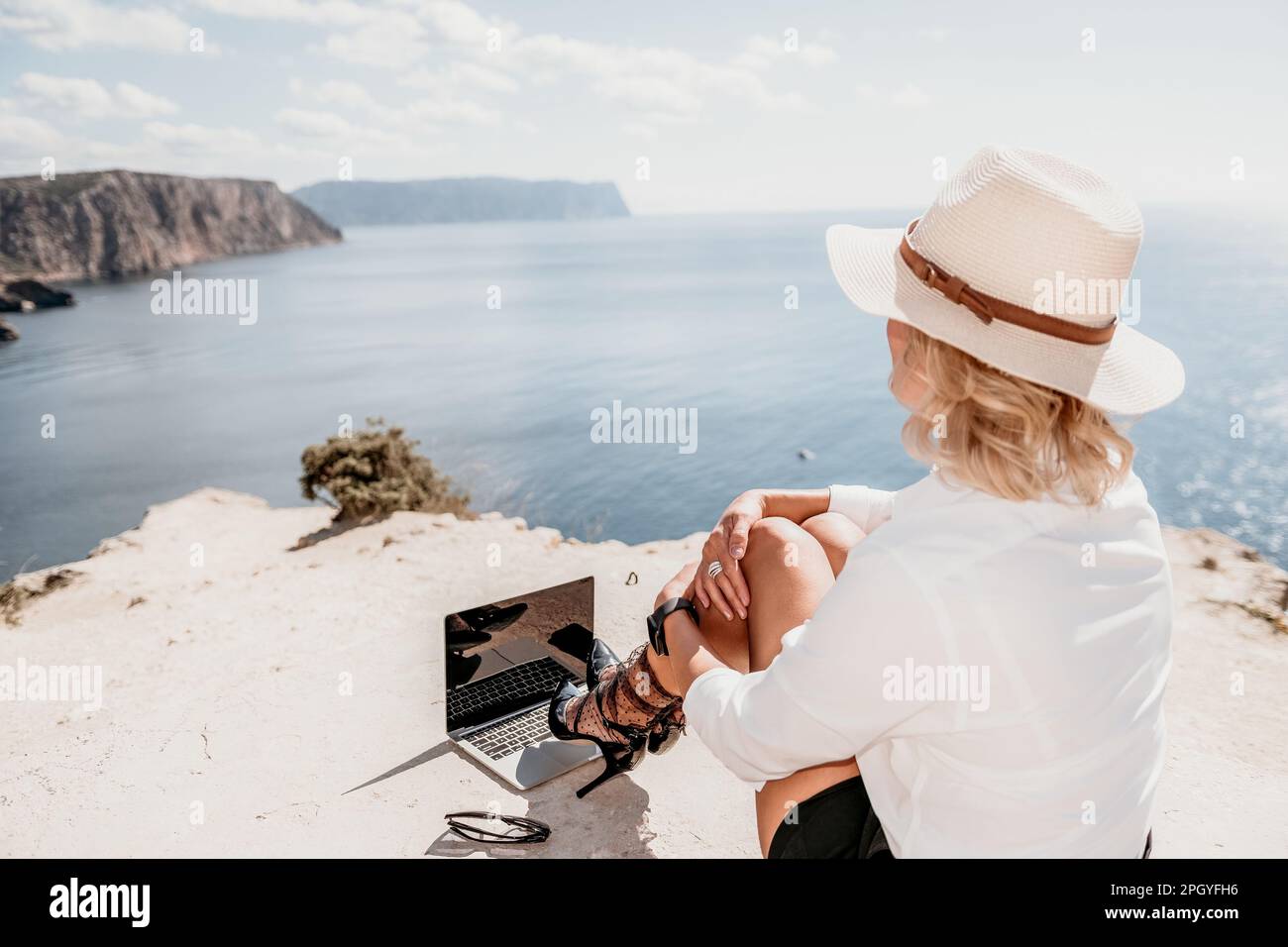 Woman sea laptop. Business woman in yellow hat freelancer with laptop working over blue sea beach. Girl relieves stress from work. Freelance, digital Stock Photo