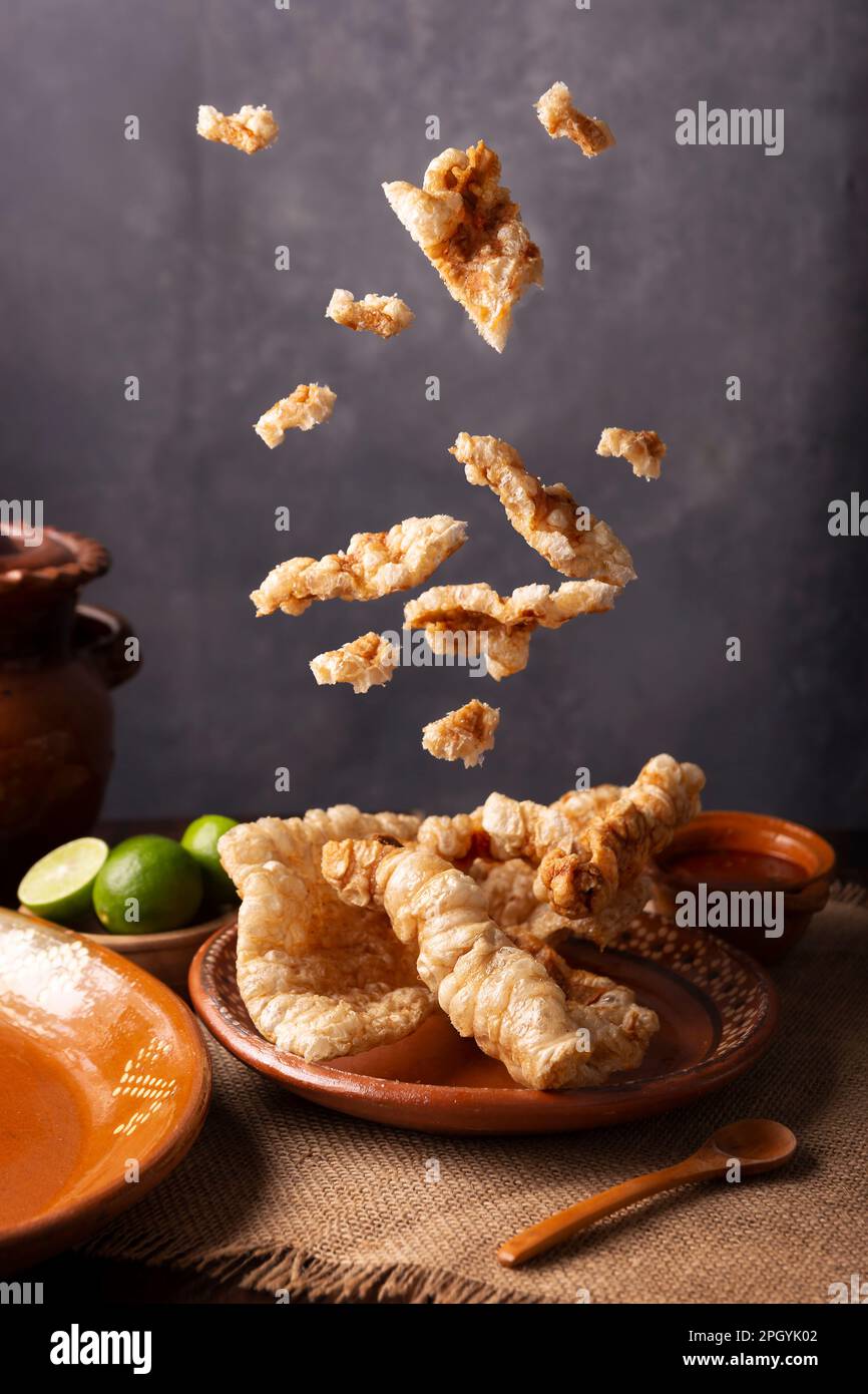 Chicharron falling on clay plate. Crispy Fried pork rind, are pieces of aired and fried pork skin, traditional Mexican ingredient or snack served with Stock Photo