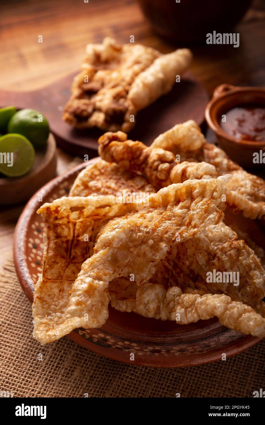 Chicharron. Crispy Fried pork rind, are pieces of aired and fried pork skin, traditional Mexican ingredient or snack served with lime juice and red ho Stock Photo