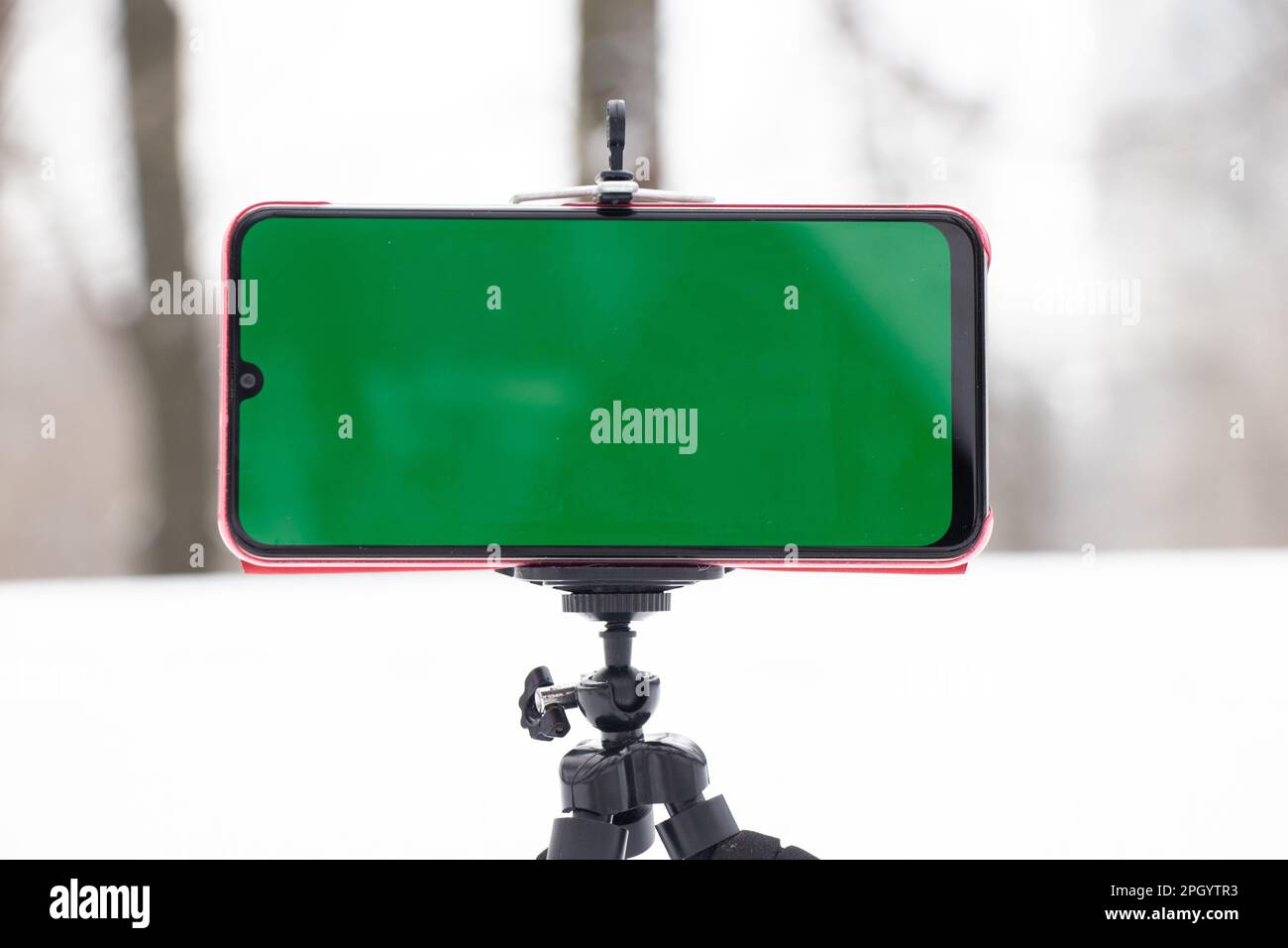a mobile phone with a green screen in winter stands on a flexible stand in the snow outside Stock Photo