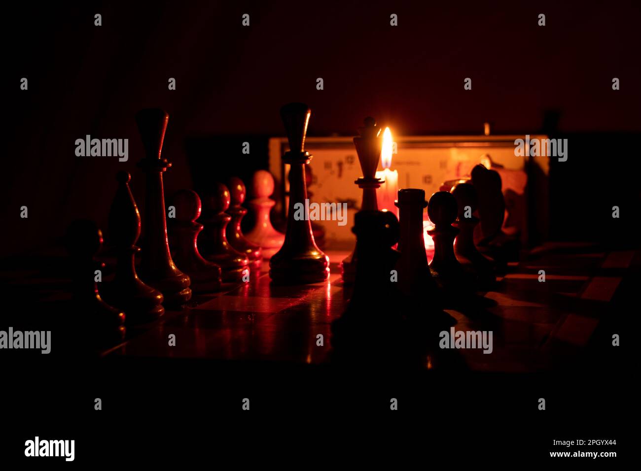 chess pieces stand on a chessboard and clock and next to a burning candle in the dark, playing chess Stock Photo