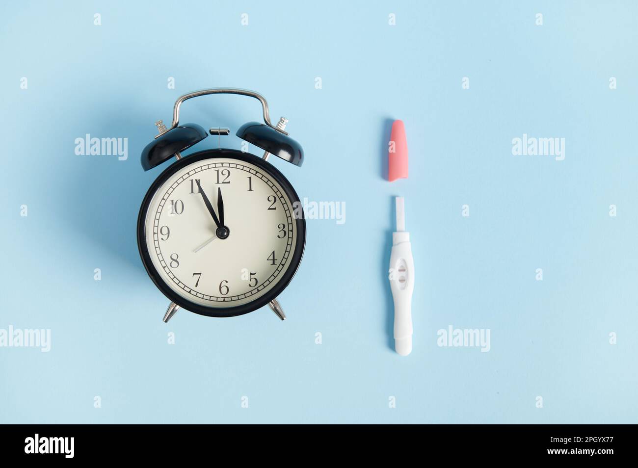 Still life alarm clock and positive inkjet pregnancy test kit showing