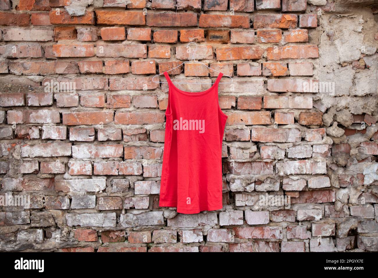 red womens dress hanging on a brick old wall outside in the sun Stock Photo