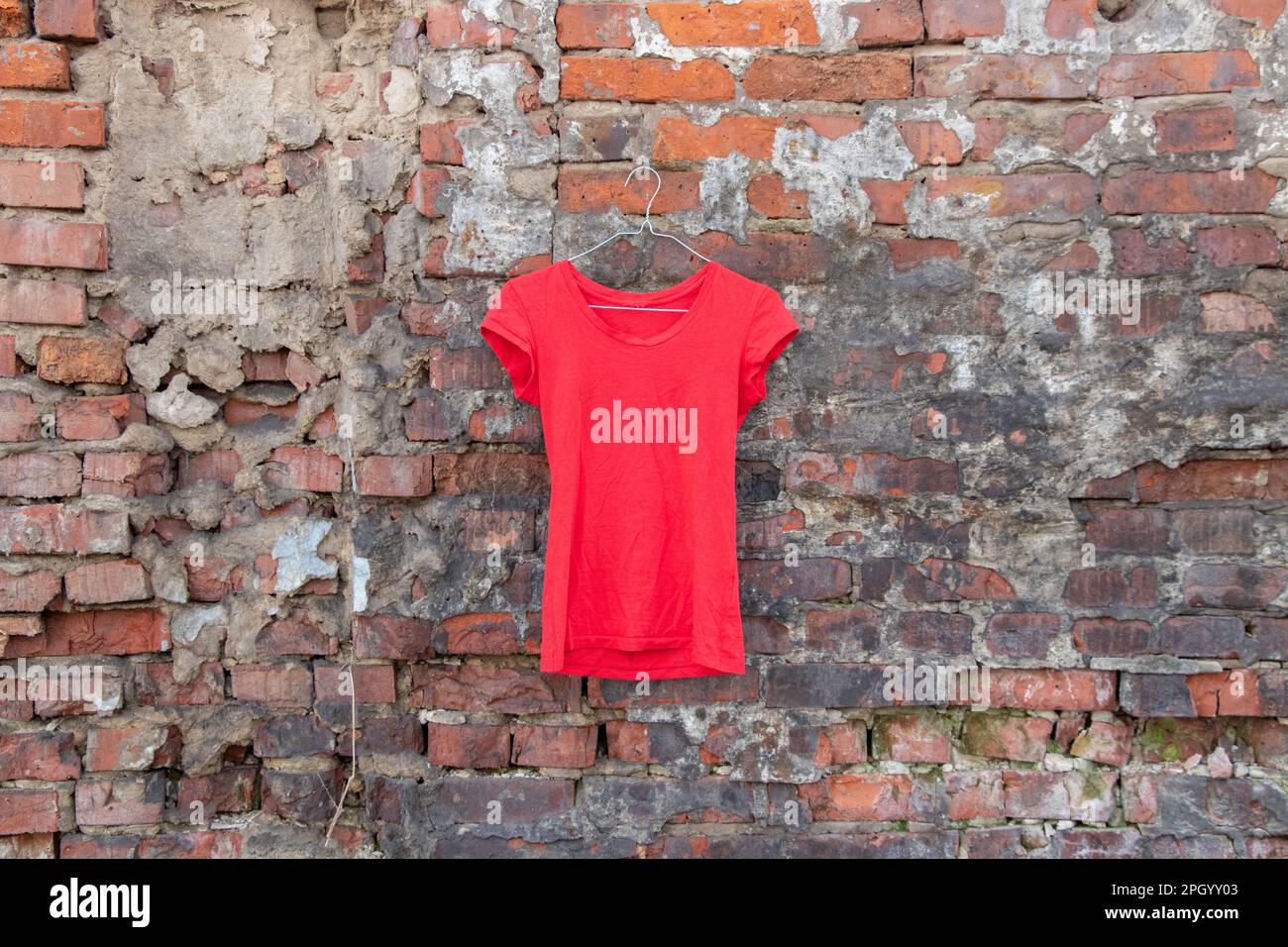 red t-shirt hanging on a hanger on a brick wall in the street, fashion womens clothing Stock Photo
