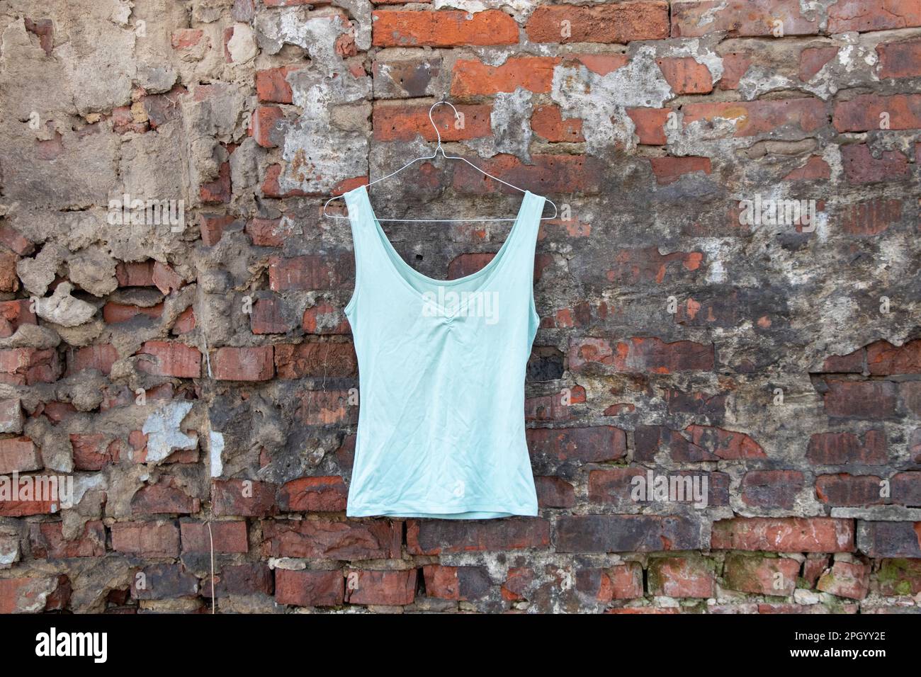 women's blue t-shirt hanging on a hanger on a brick wall in the street, women's clothing Stock Photo