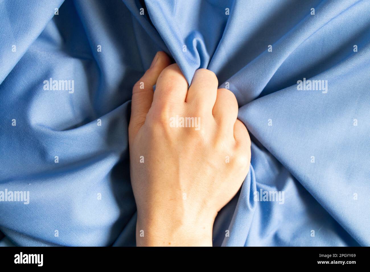 female hand clenches a blue cloth into a fist, hand in a fist, power anger Stock Photo