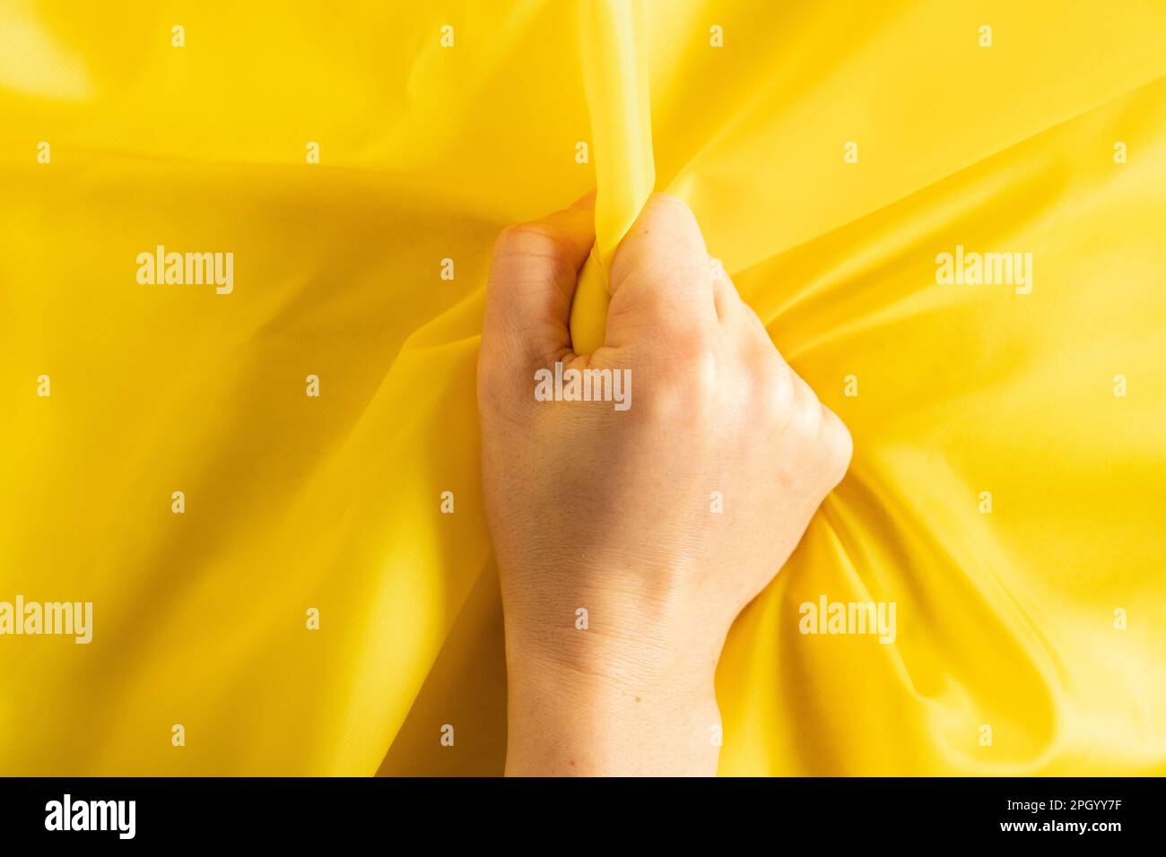 female hand clenches yellow cloth into a fist, hand in a fist, power anger Stock Photo