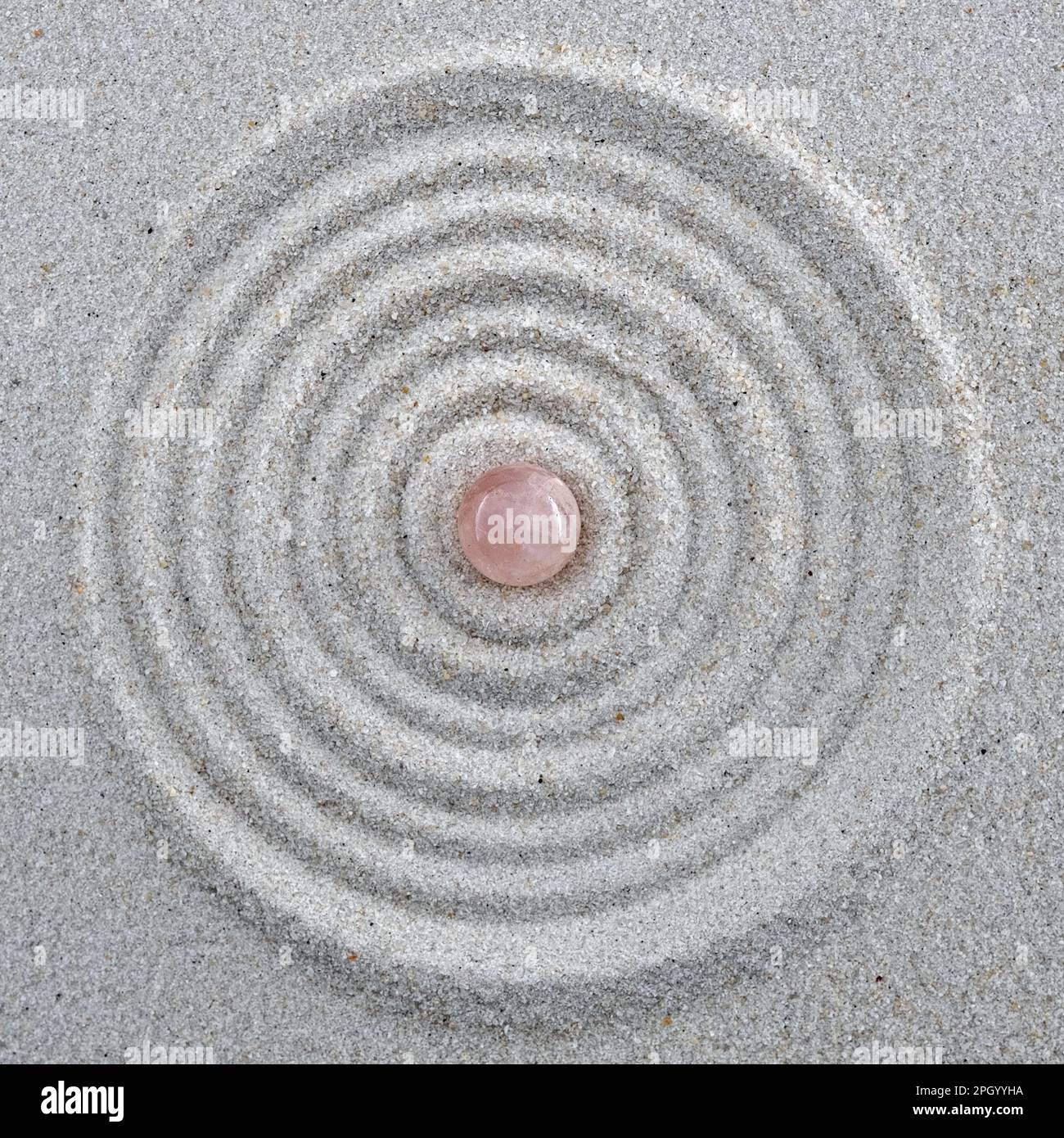 rose quartz sphere in the middle of circles drawn in sand, spa, zen