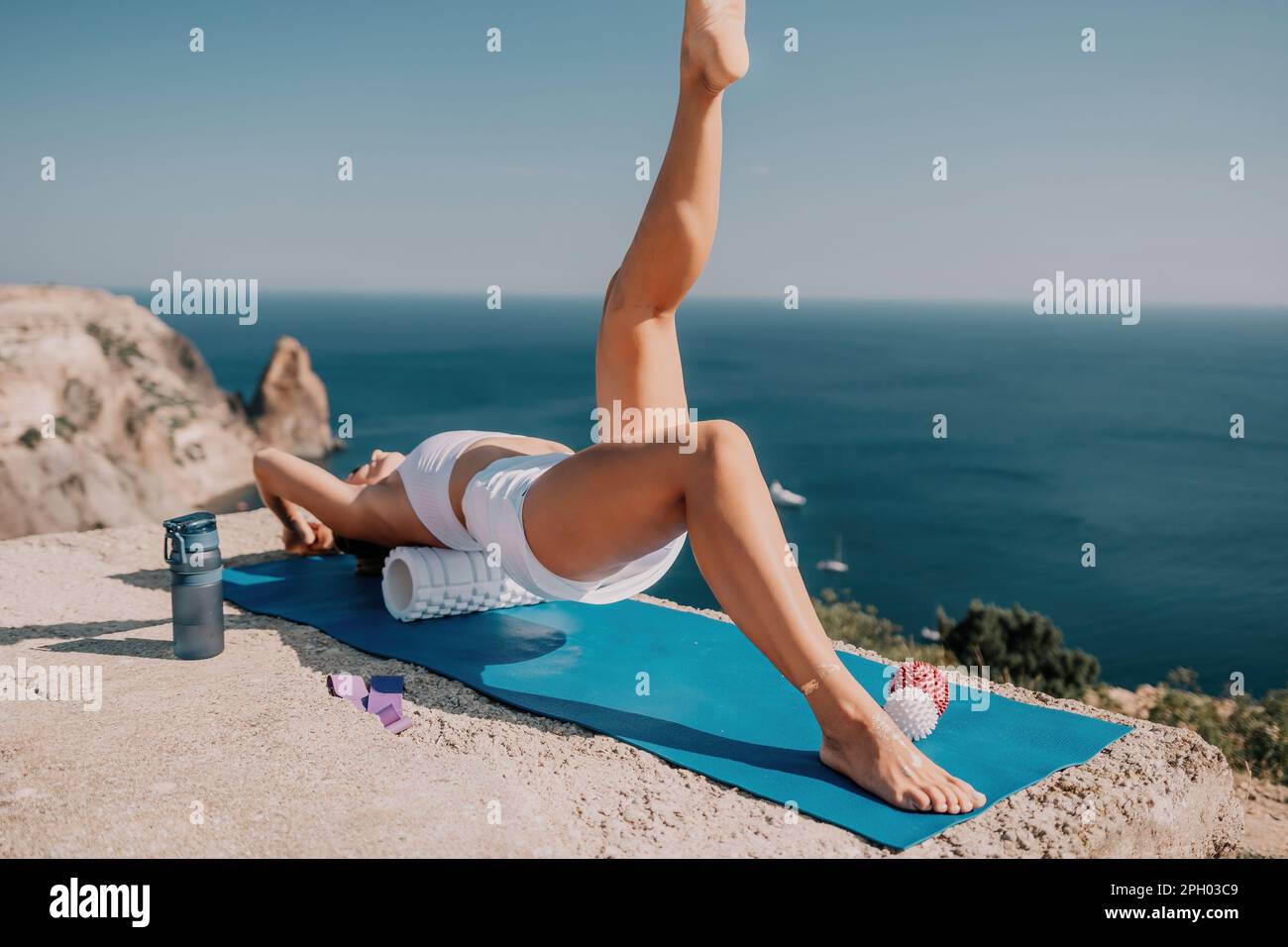 Woman sea pilates. Sporty happy middle aged woman practicing fitness on yoga mat with balls and roller near sea, smiling active female outside Stock Photo